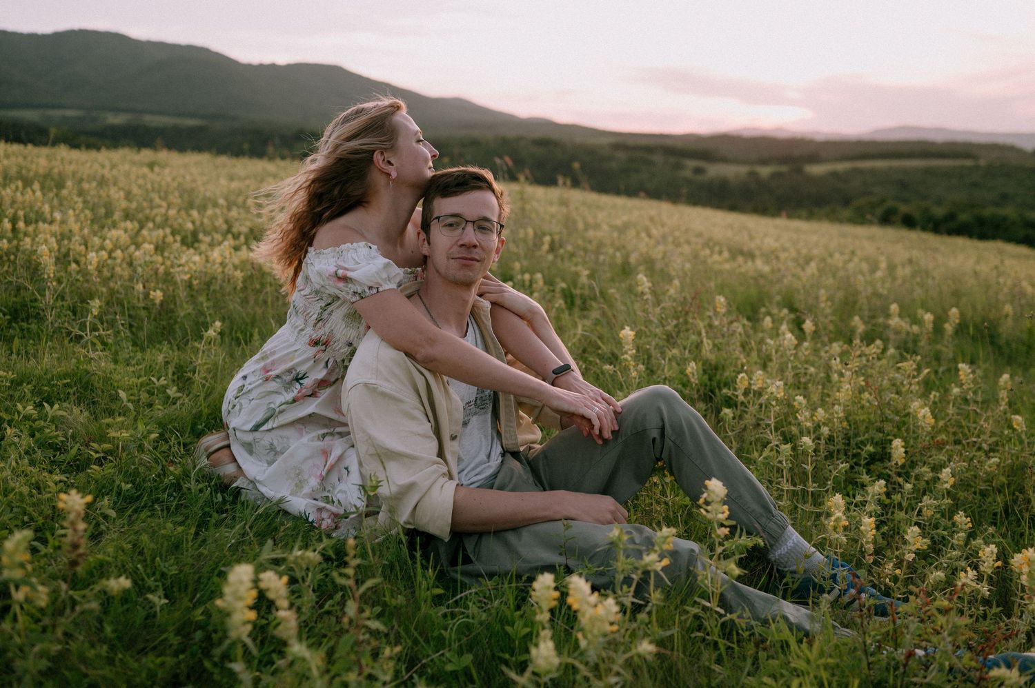 Playful couple enjoying sunset in mountain meadow filled with yellow wildflowers.