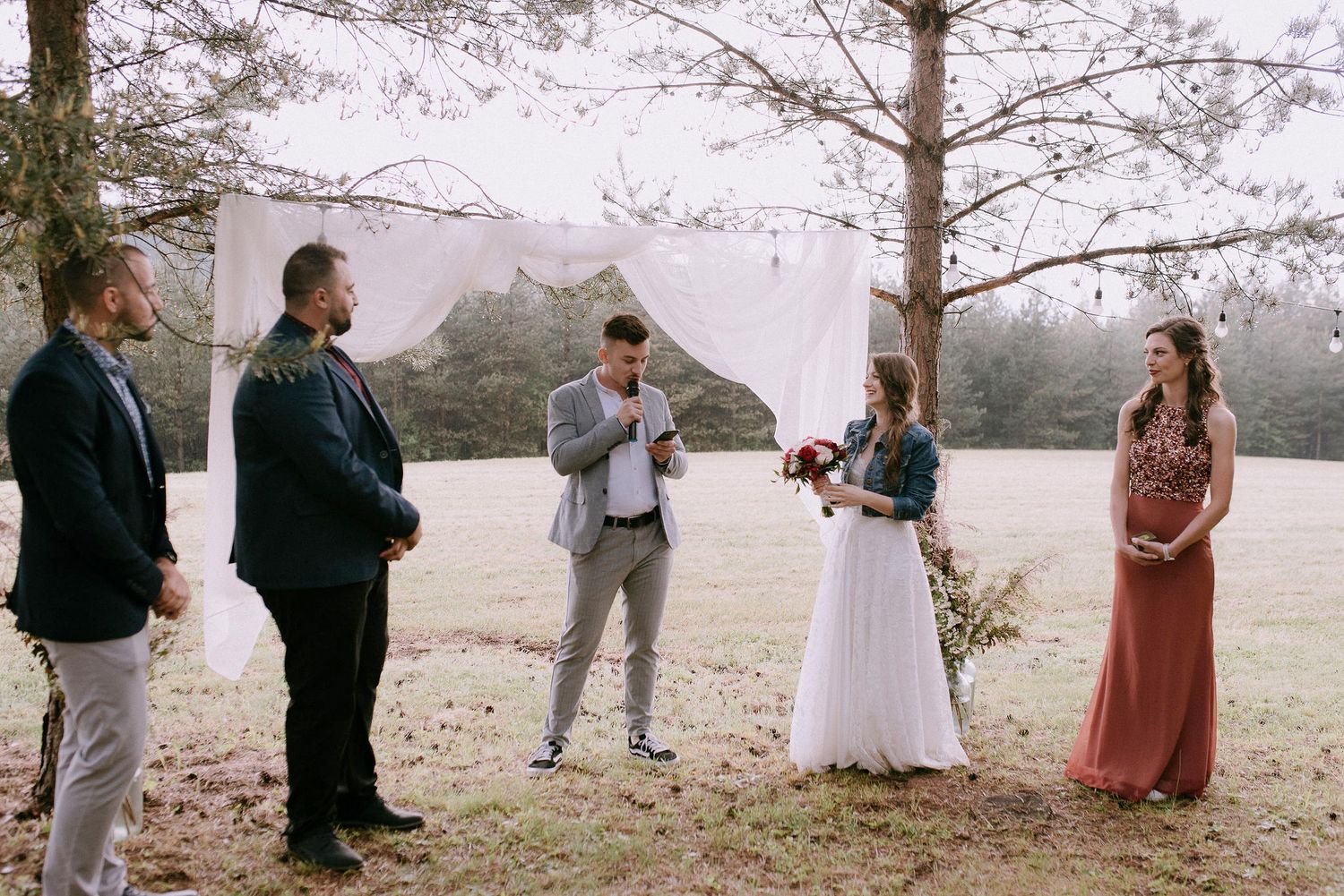 Natural outdoor wedding ceremony with guests gathered under pine trees.