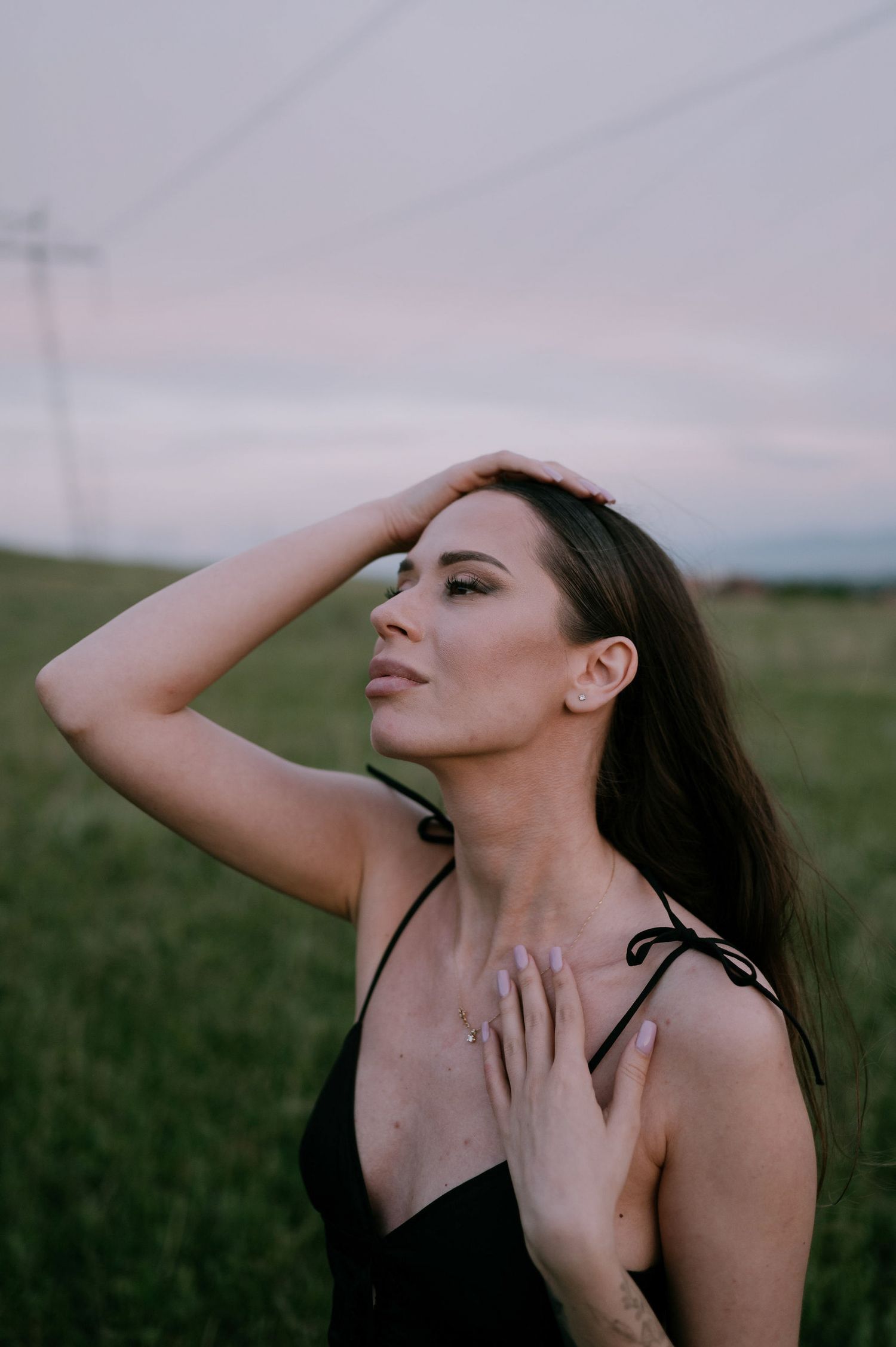 A woman poses expressively in a field at sunset with dramatic gestures and movements.