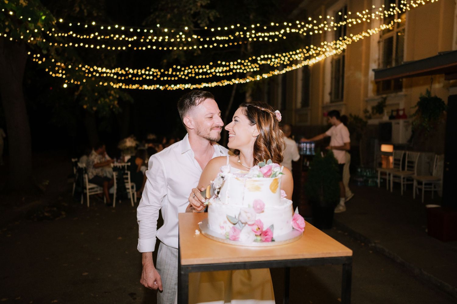 A romantic evening wedding reception with string lights illuminating the outdoor dance floor and guests dancing.