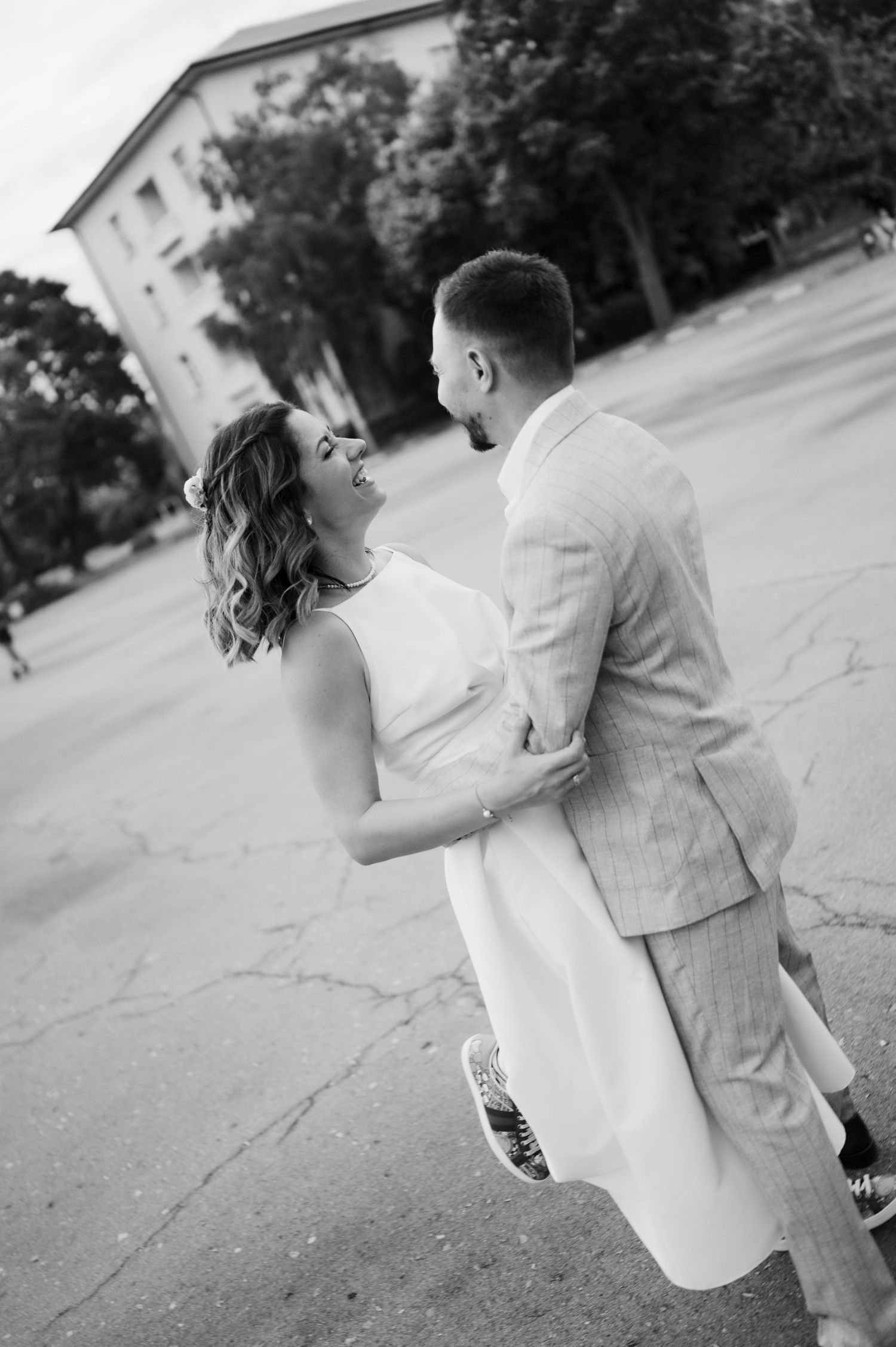 A couple in wedding attire share a playful and romantic moment outdoors in black and white photography.