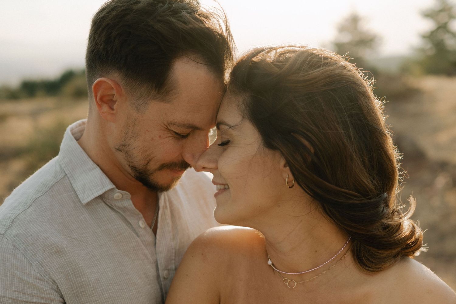 Romantic couple embraces during golden hour photoshoot in a natural outdoor setting.