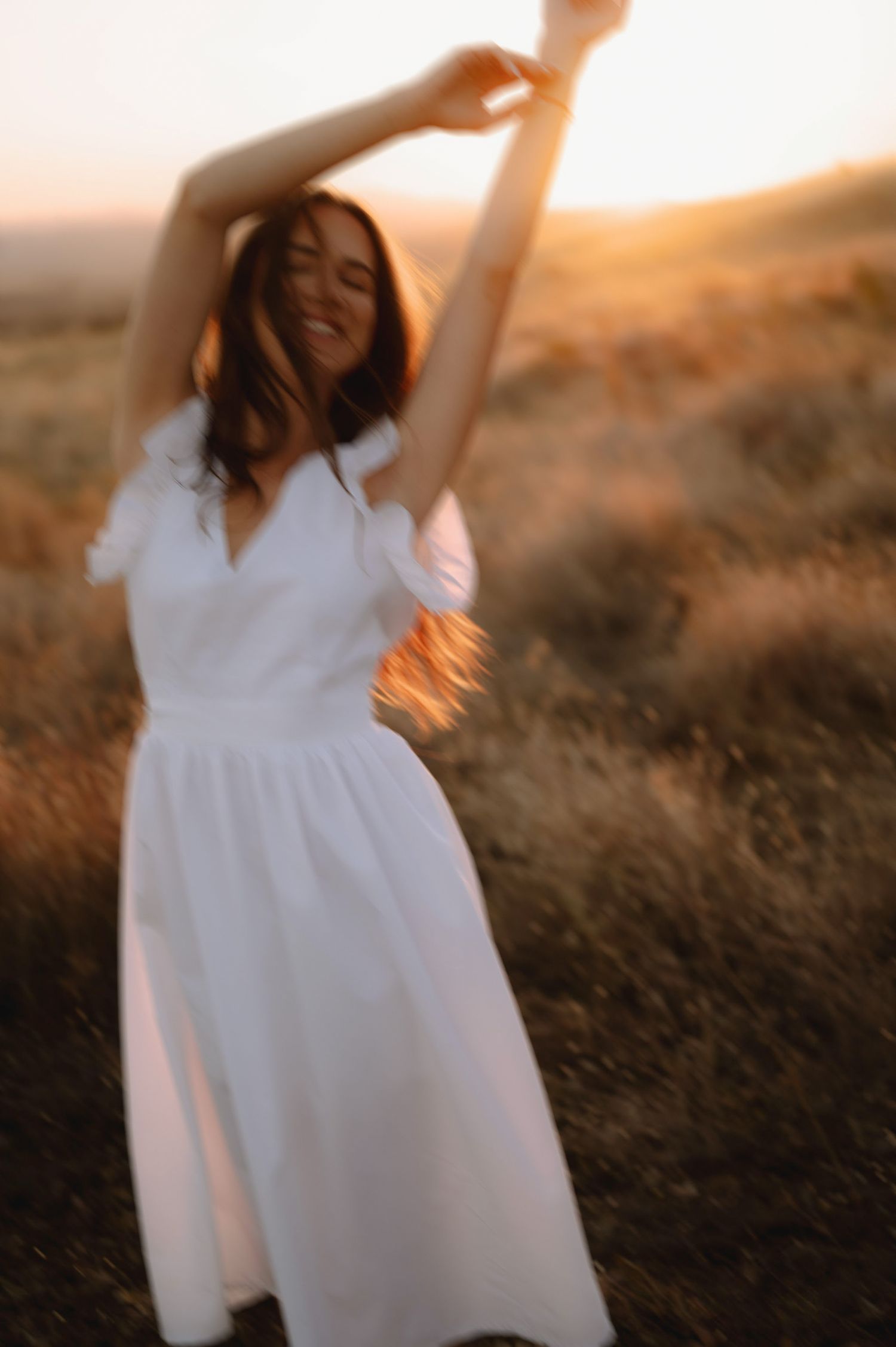 A figure in a flowing white dress dances gracefully in a golden field at sunset, creating a dreamy ethereal scene.