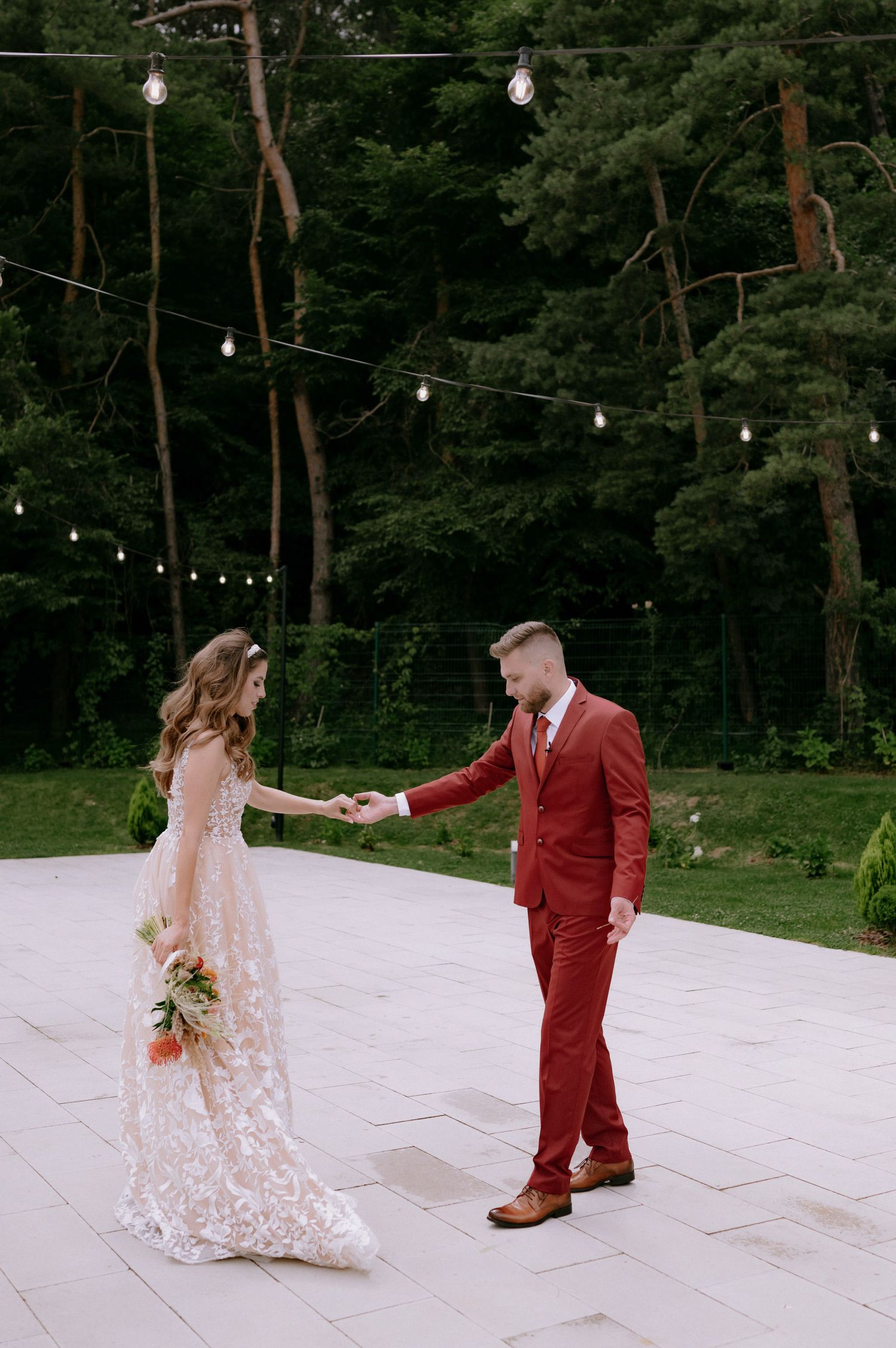 A couple dances on a stone patio with string lights hanging overhead in a romantic garden setting.
