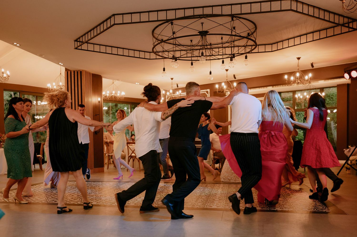 Dance class participants practicing choreography together in a mirrored studio with hardwood floors and circular lighting fixtures.