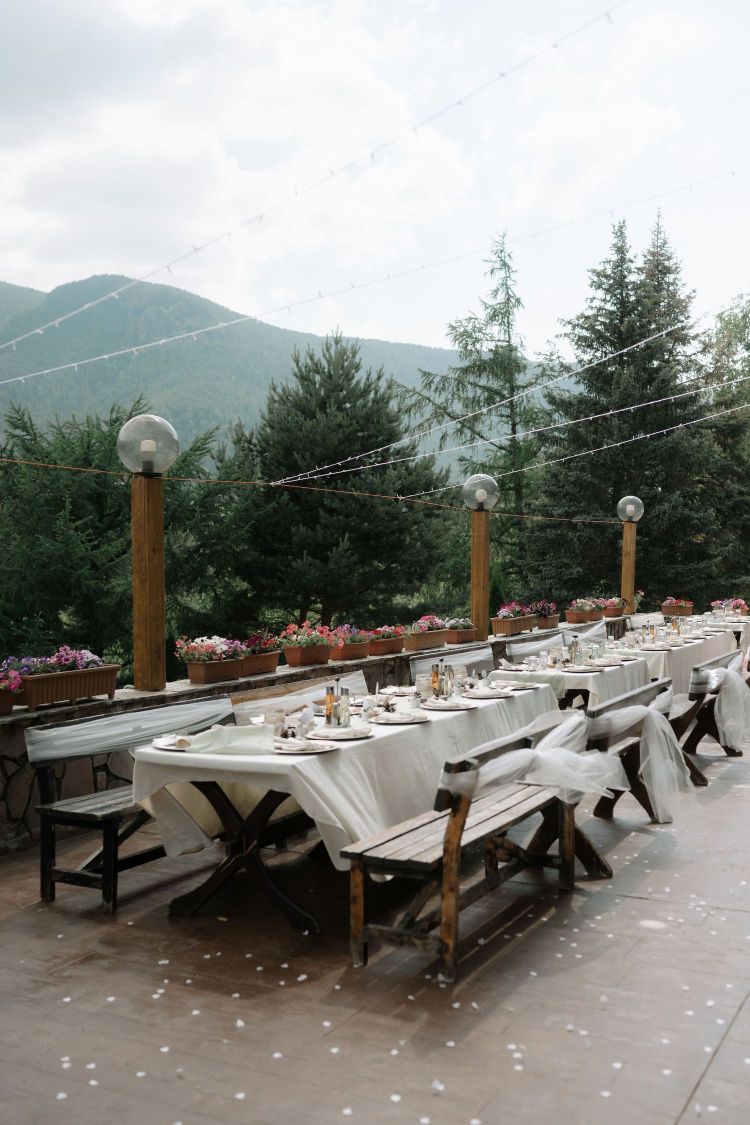 Outdoor wedding reception tables with white linens and wooden posts set against a misty mountain backdrop.