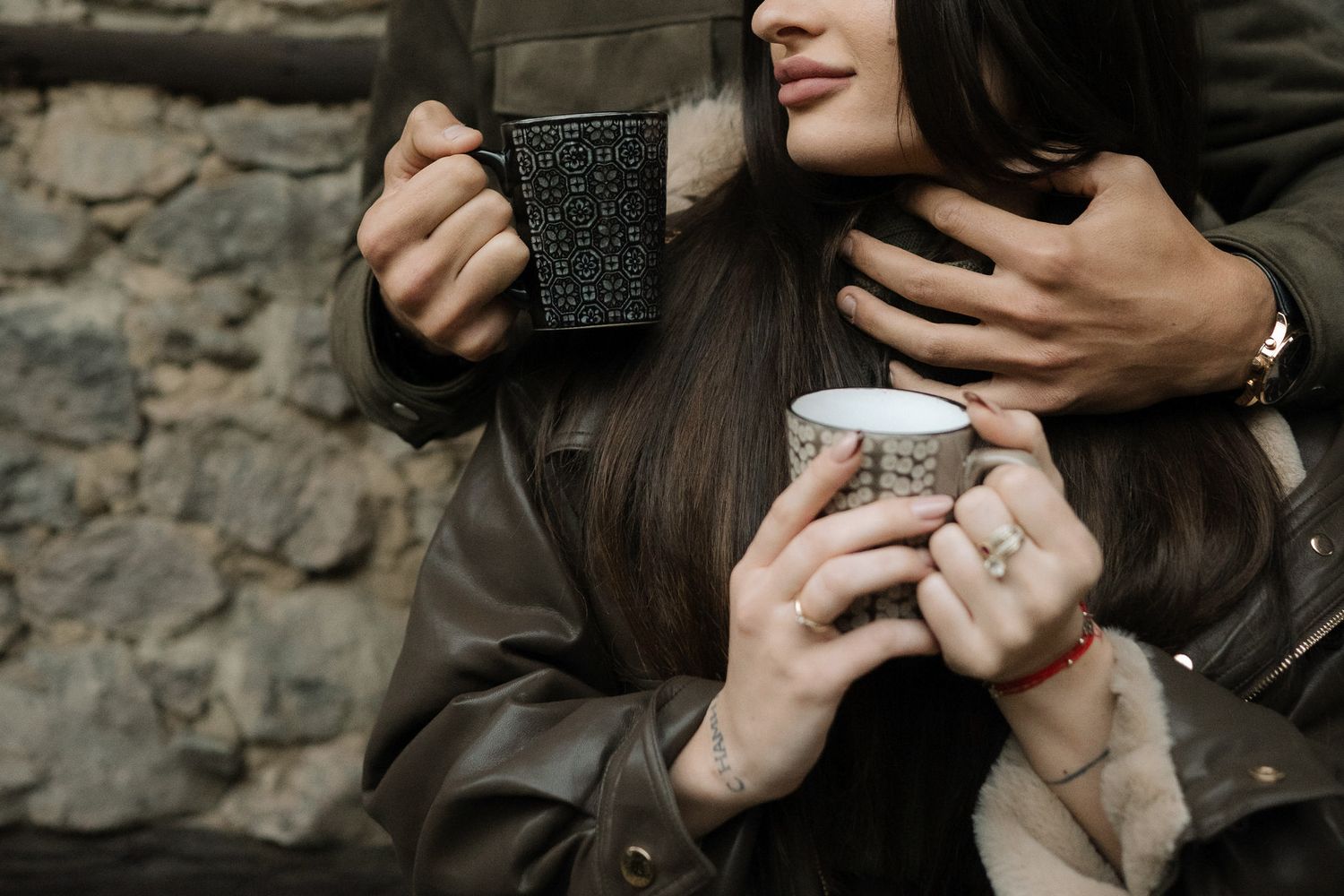 Close-up shots of hands holding disposable coffee cups against a stone wall background.