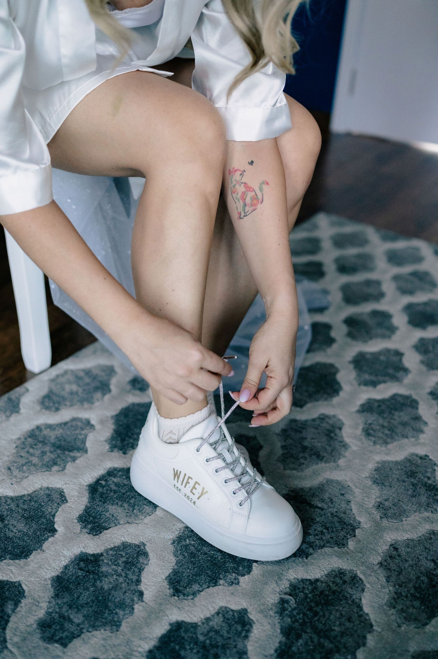 Close-up sequence of hands tying white laces on classic white canvas sneakers on a patterned blue carpet.