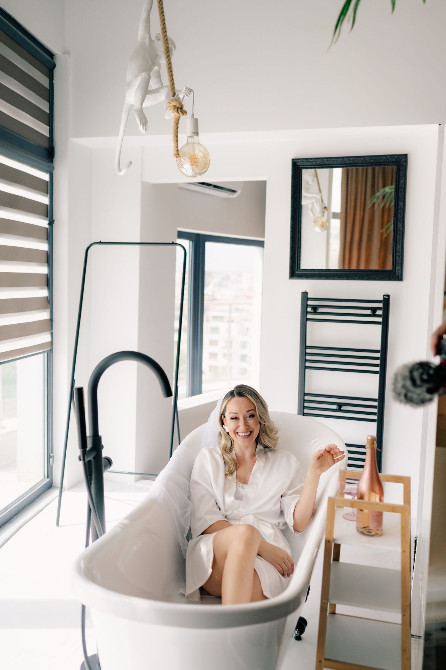 Relaxing bathroom scene with white freestanding tub, striped window shades, and hanging rope pendant light.