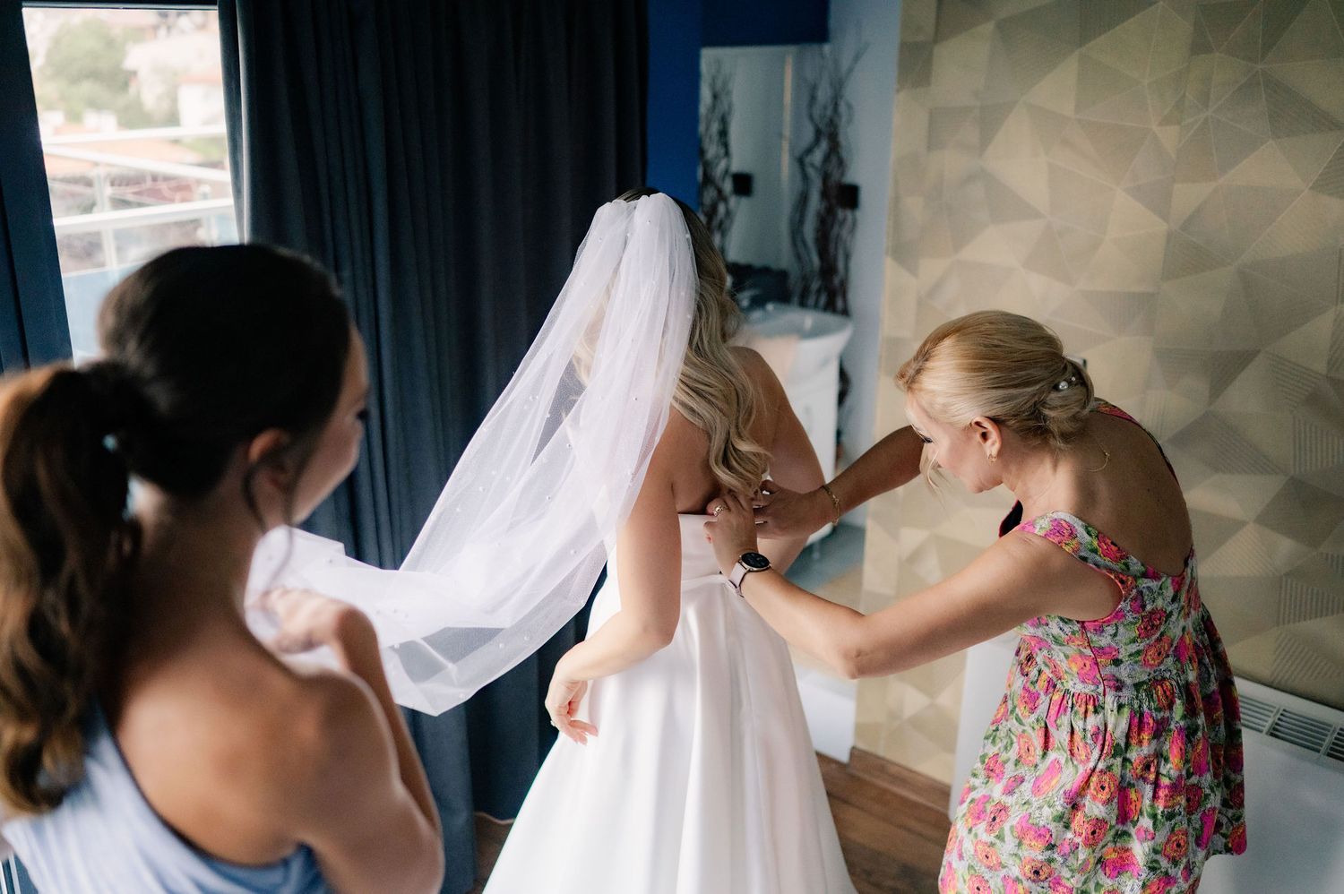 A bride getting ready for her wedding with bridesmaids in floral dresses helping with final preparations.