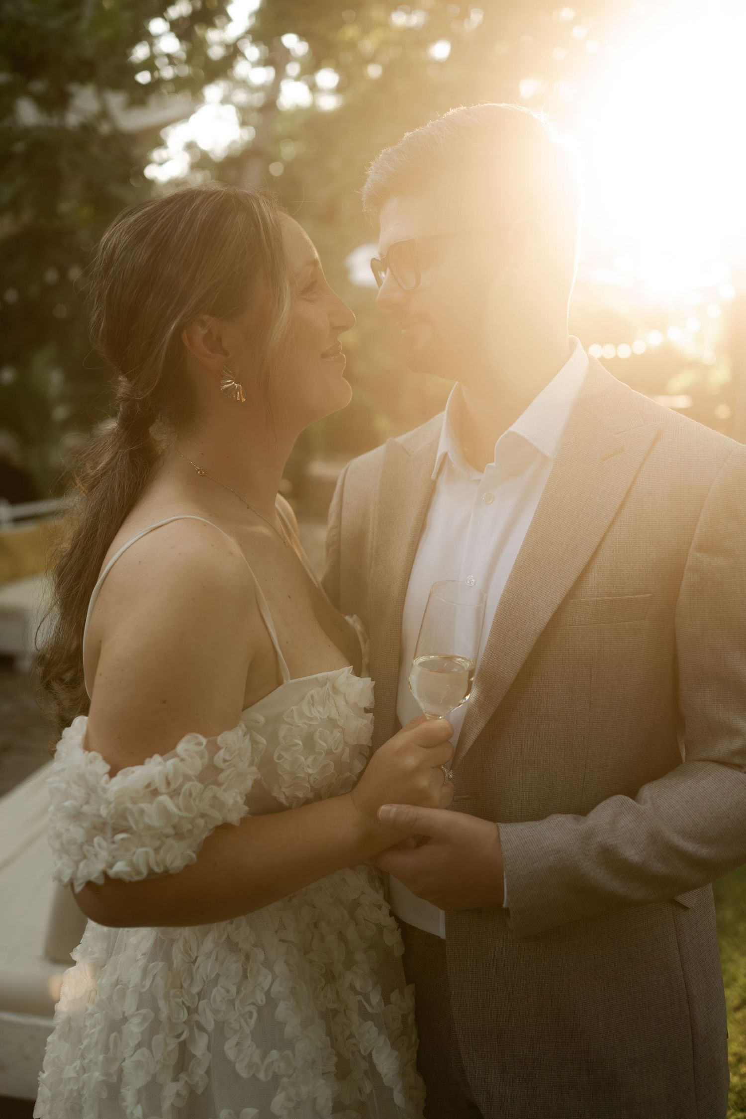 A romantic wedding couple embraces in golden sunlight during sunset creating a dreamy silhouette effect.