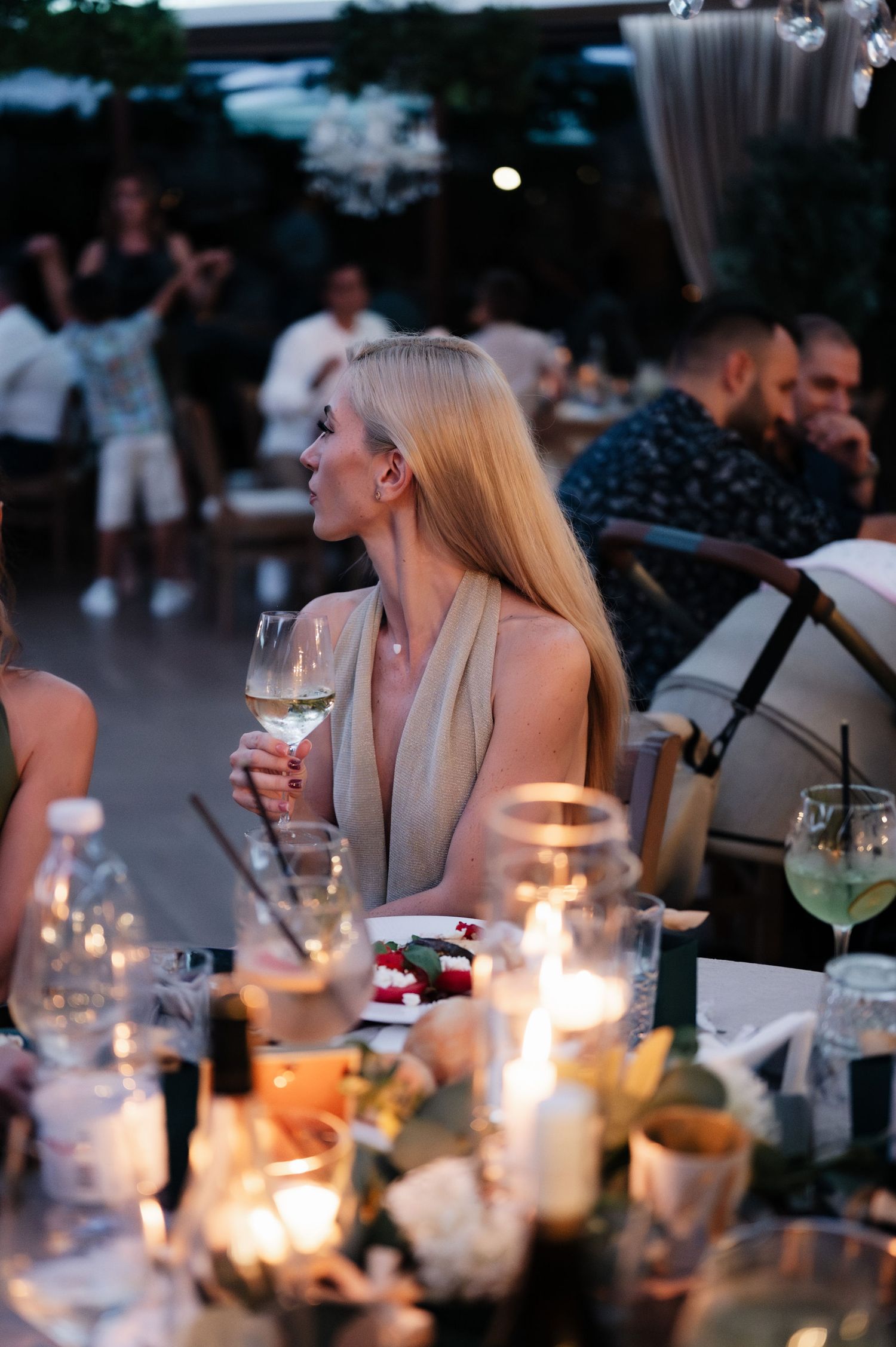 People enjoying dinner and drinks at a candlelit outdoor table during twilight hours.