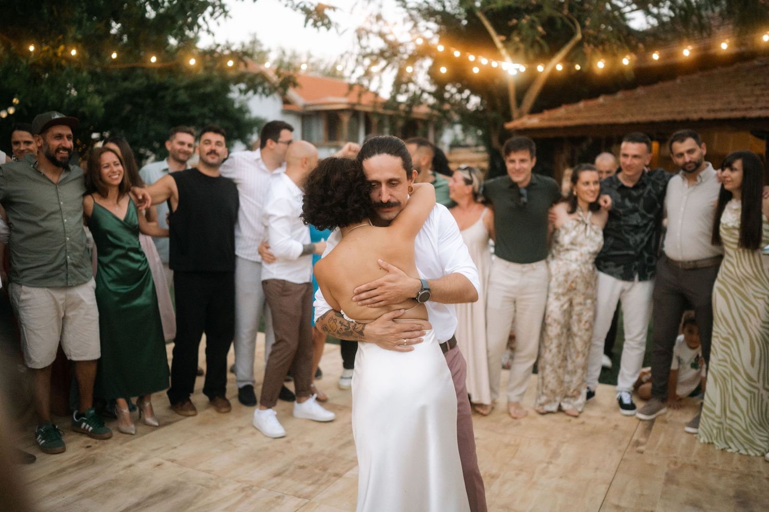 Wedding guests dance and celebrate during an outdoor evening reception with string lights overhead.