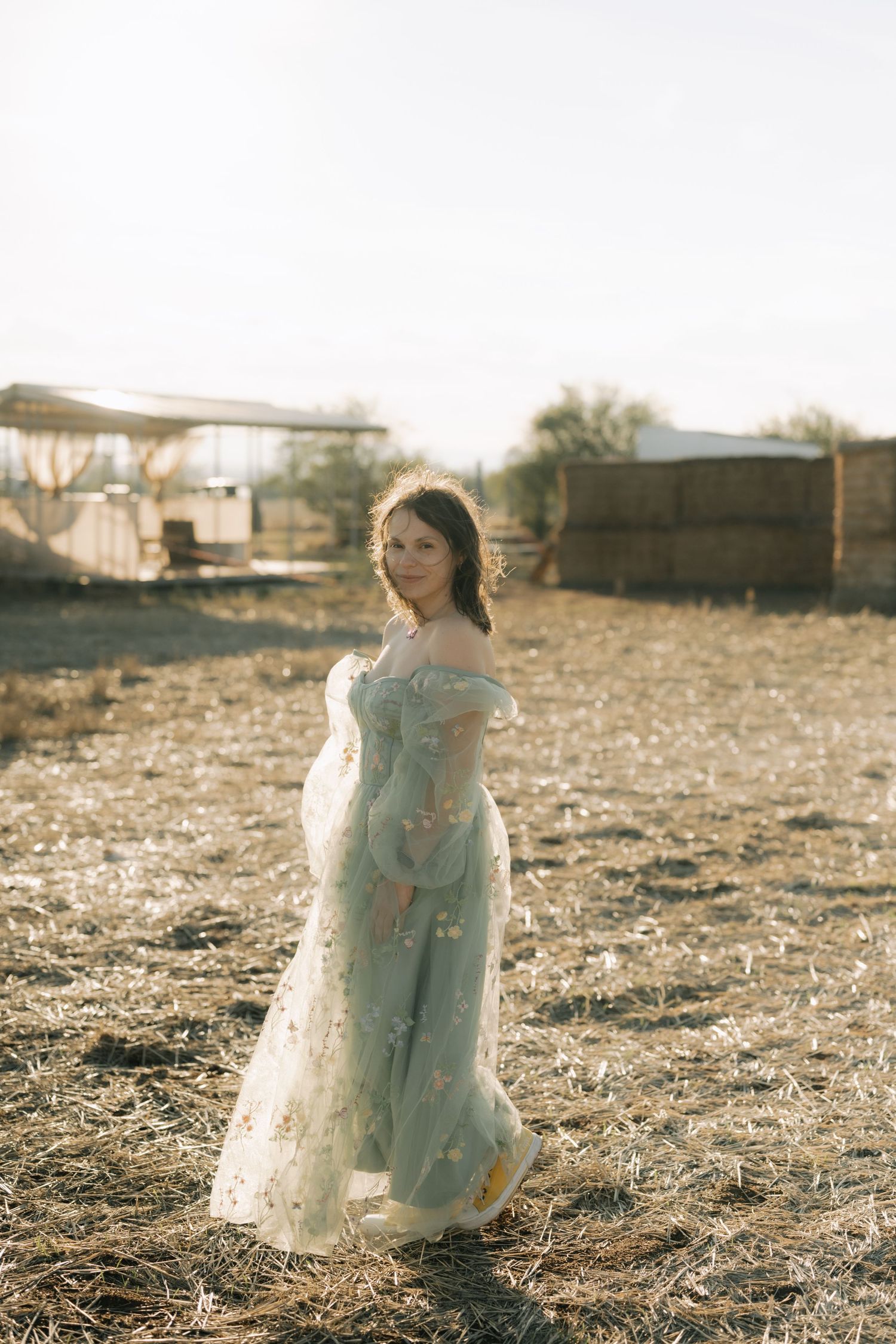 A person in a flowing white dress sits in a field at sunset creating a dreamy ethereal scene.