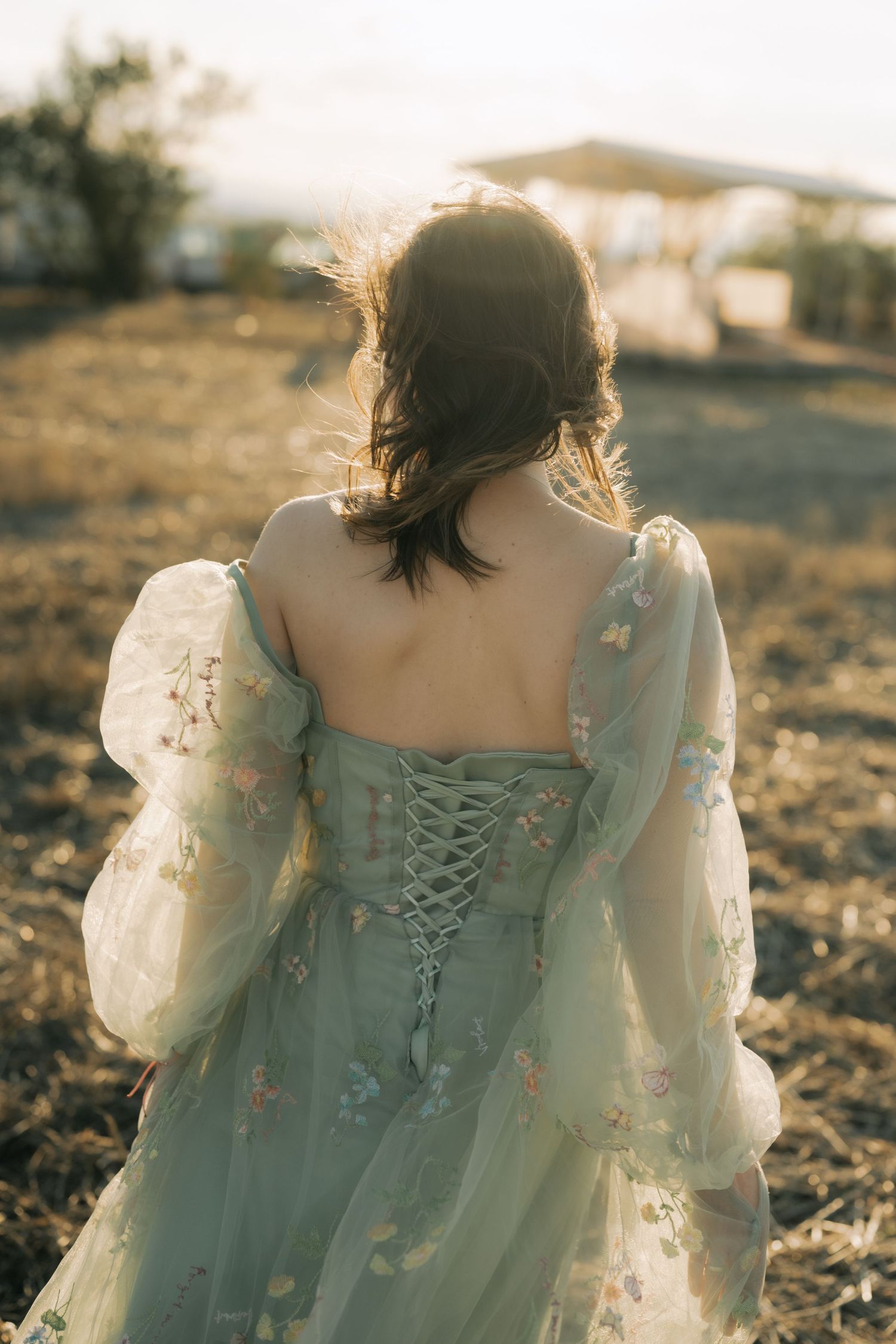 A person in a romantic vintage dress with corset lacing stands in golden sunlight at sunset.