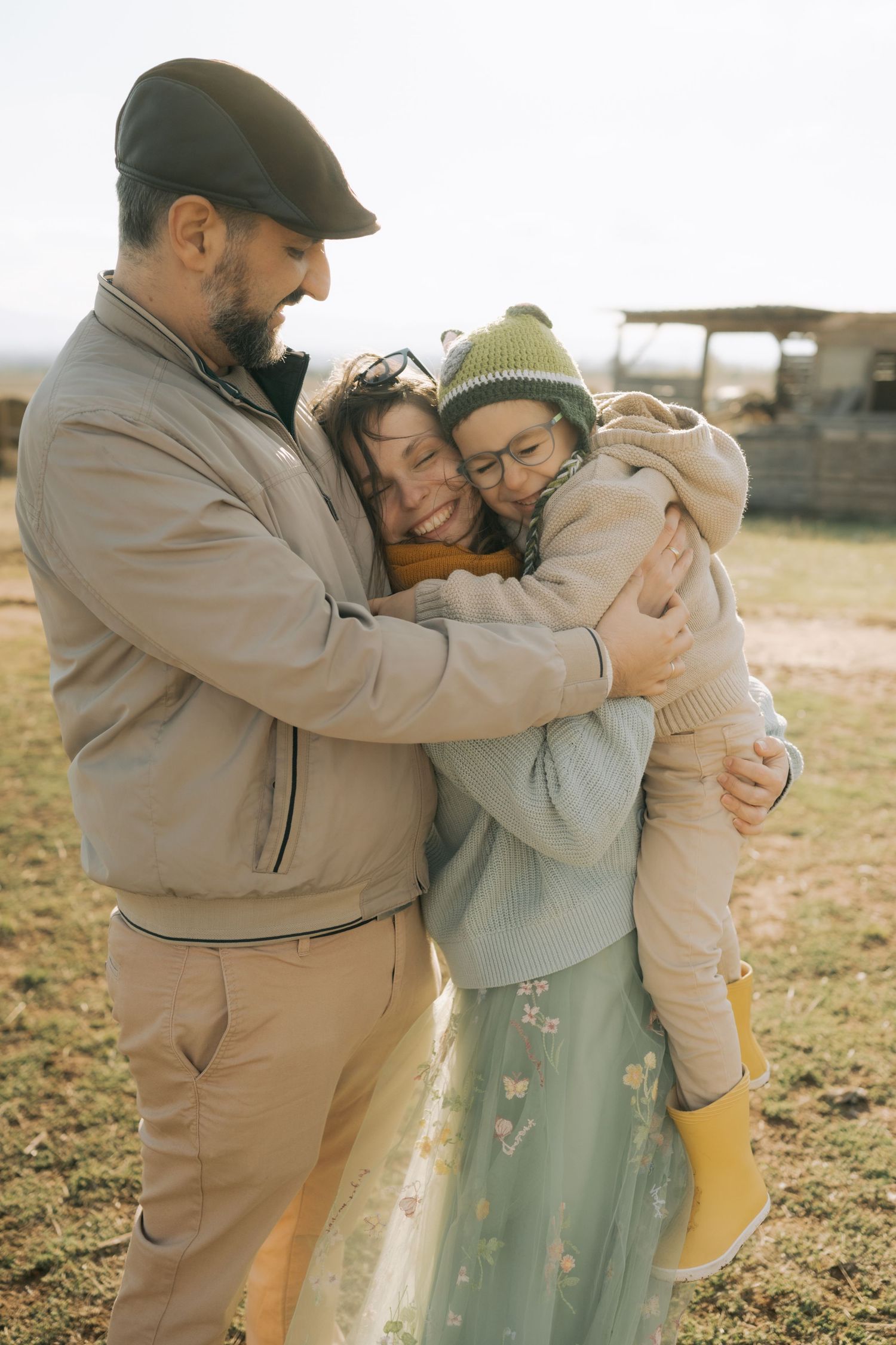 A family shares tender embraces outdoors during a warm sunset photoshoot in casual attire.