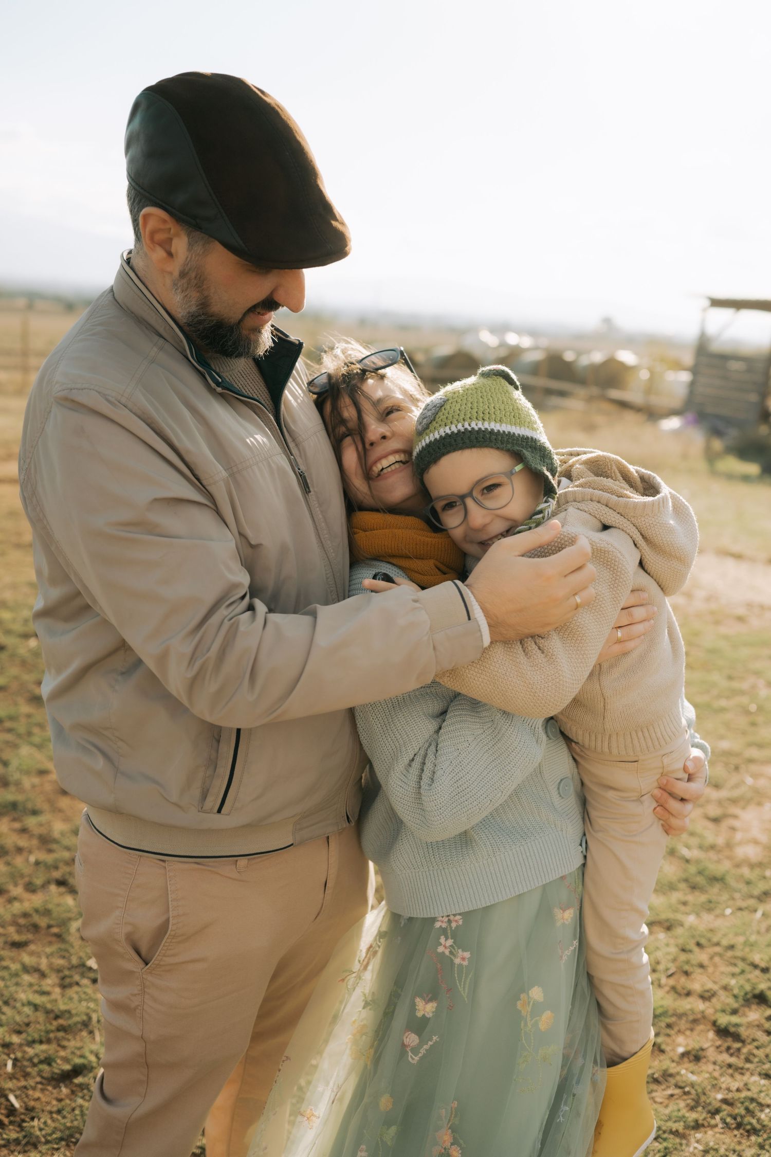 A couple embraces tenderly in a field during golden hour while wearing casual earth-toned clothing.