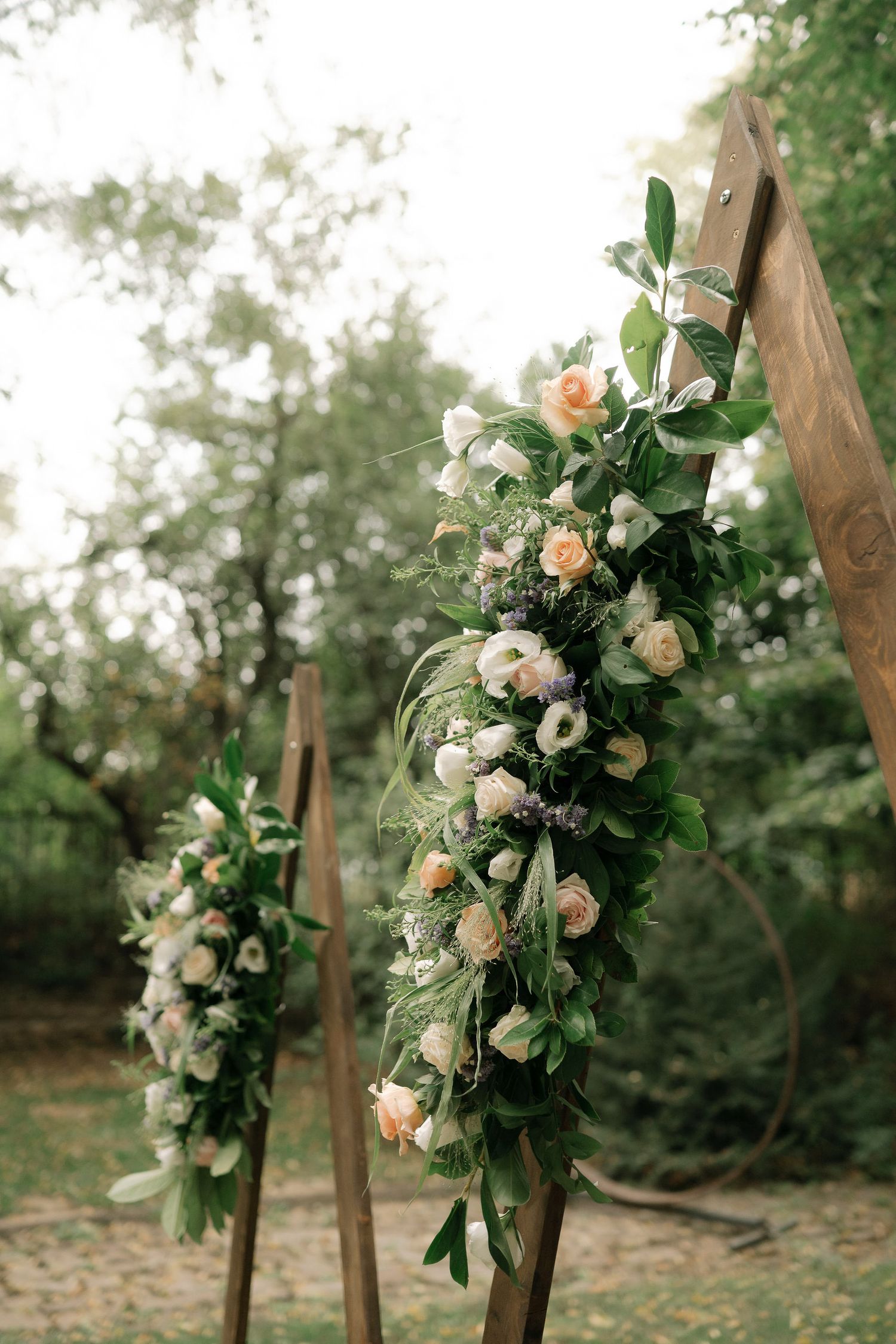 Beautiful floral arrangement with peach roses and white blooms cascading down wooden wedding arch posts in outdoor garden setting.