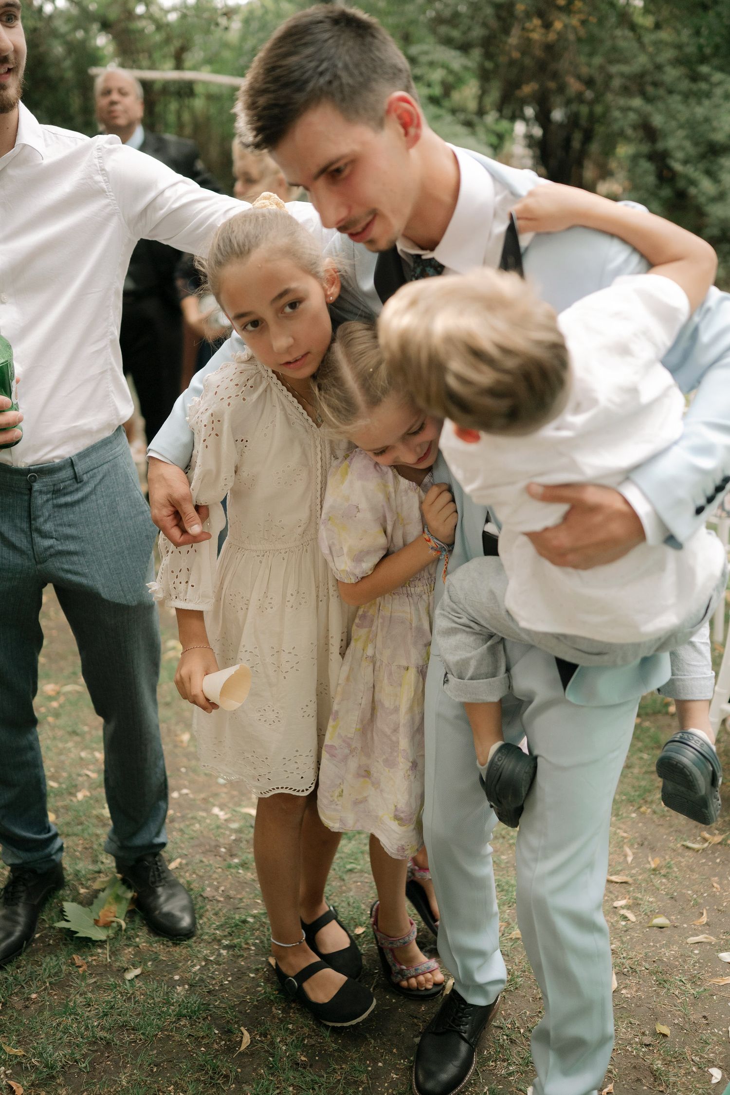 Children playing and leaning forward together during an outdoor wedding celebration.