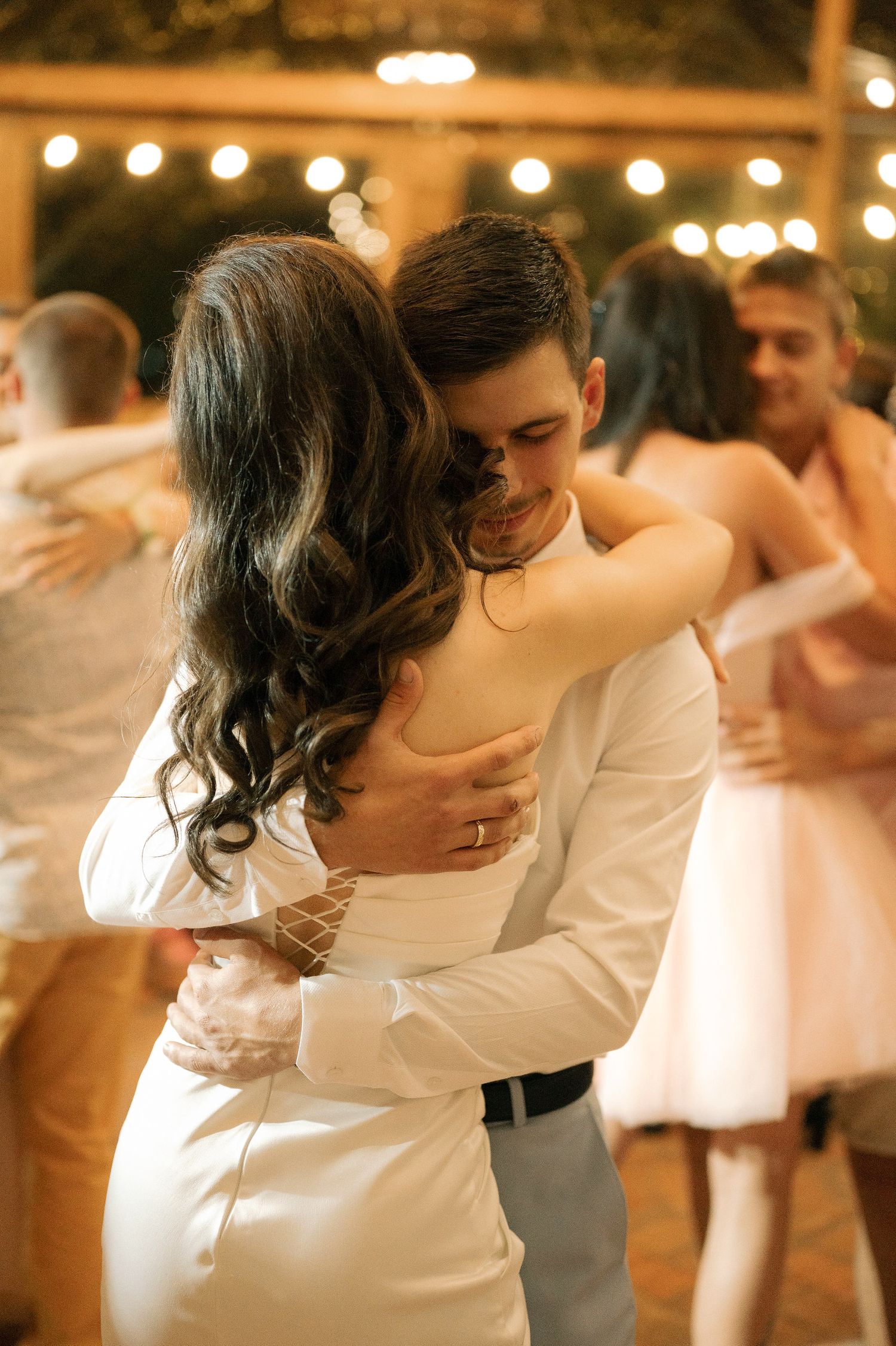 Couple shares an intimate dance moment at a wedding reception with string lights glowing in the background.