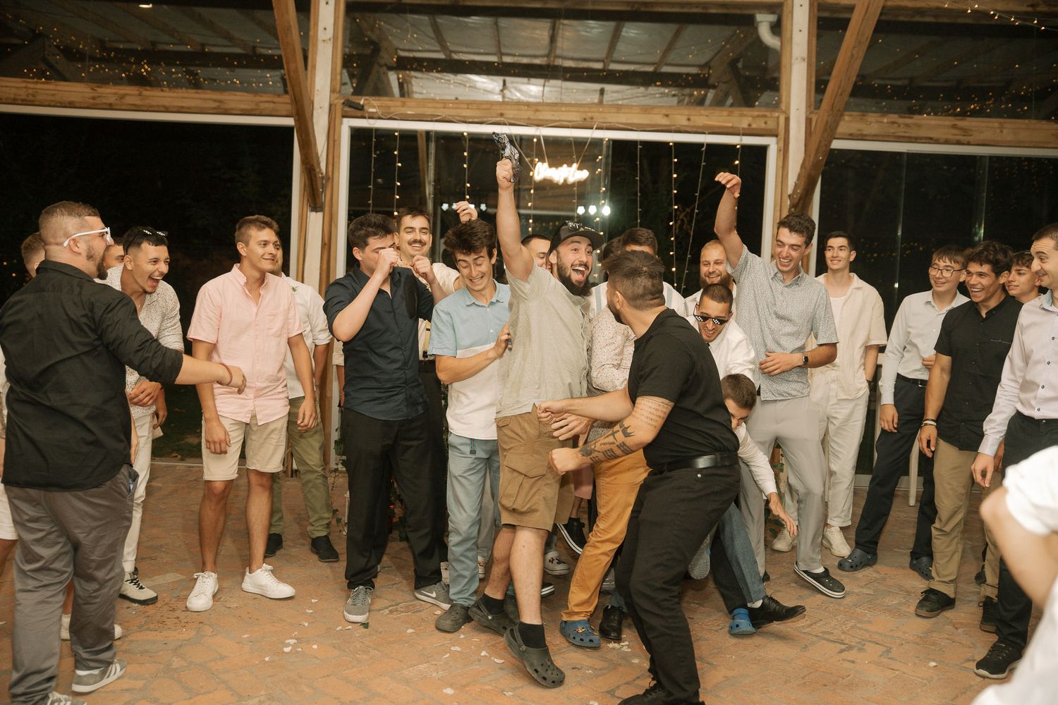 A crowd of people gather and dance in a rustic wooden barn venue during a celebration.