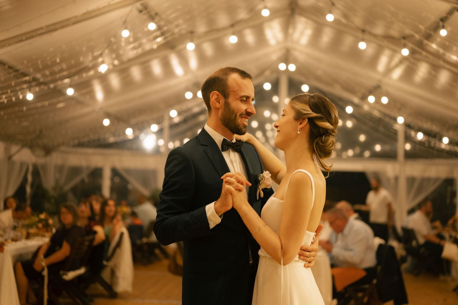 A couple shares their first dance under twinkling lights in an elegant wedding reception tent.
