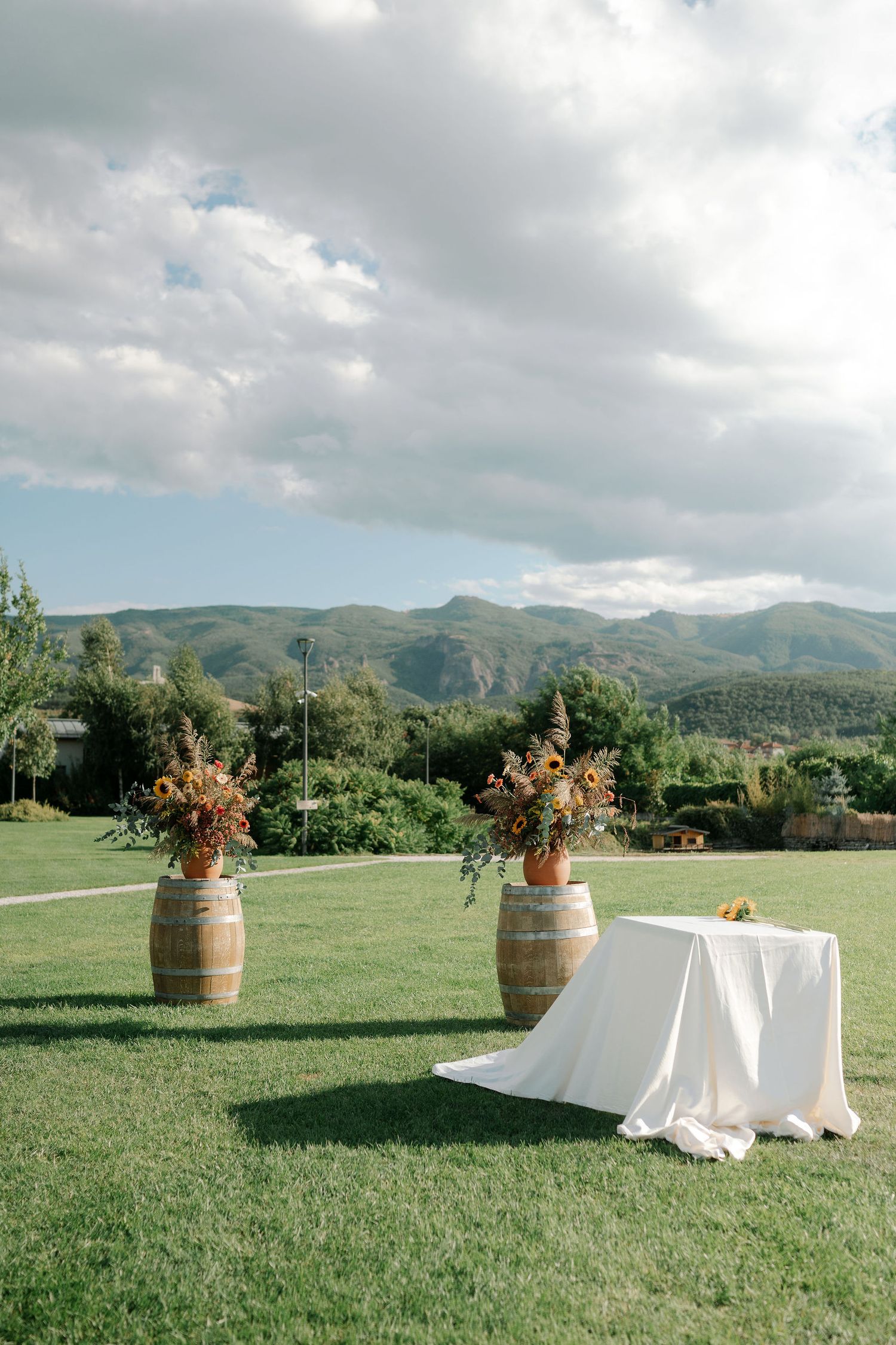 A scenic outdoor wedding setup with wine barrels and floral arrangements against a mountain landscape backdrop.