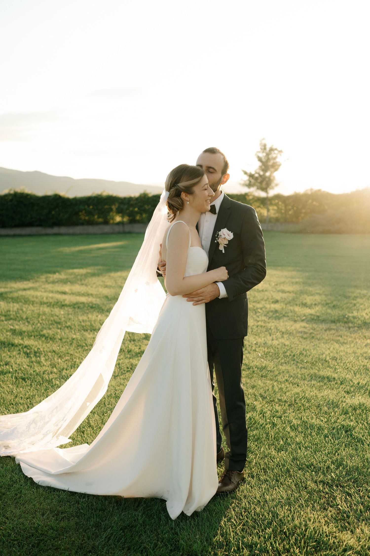 A romantic sunset wedding portrait shows a couple embracing on a lush green golf course with flowing white veil details.