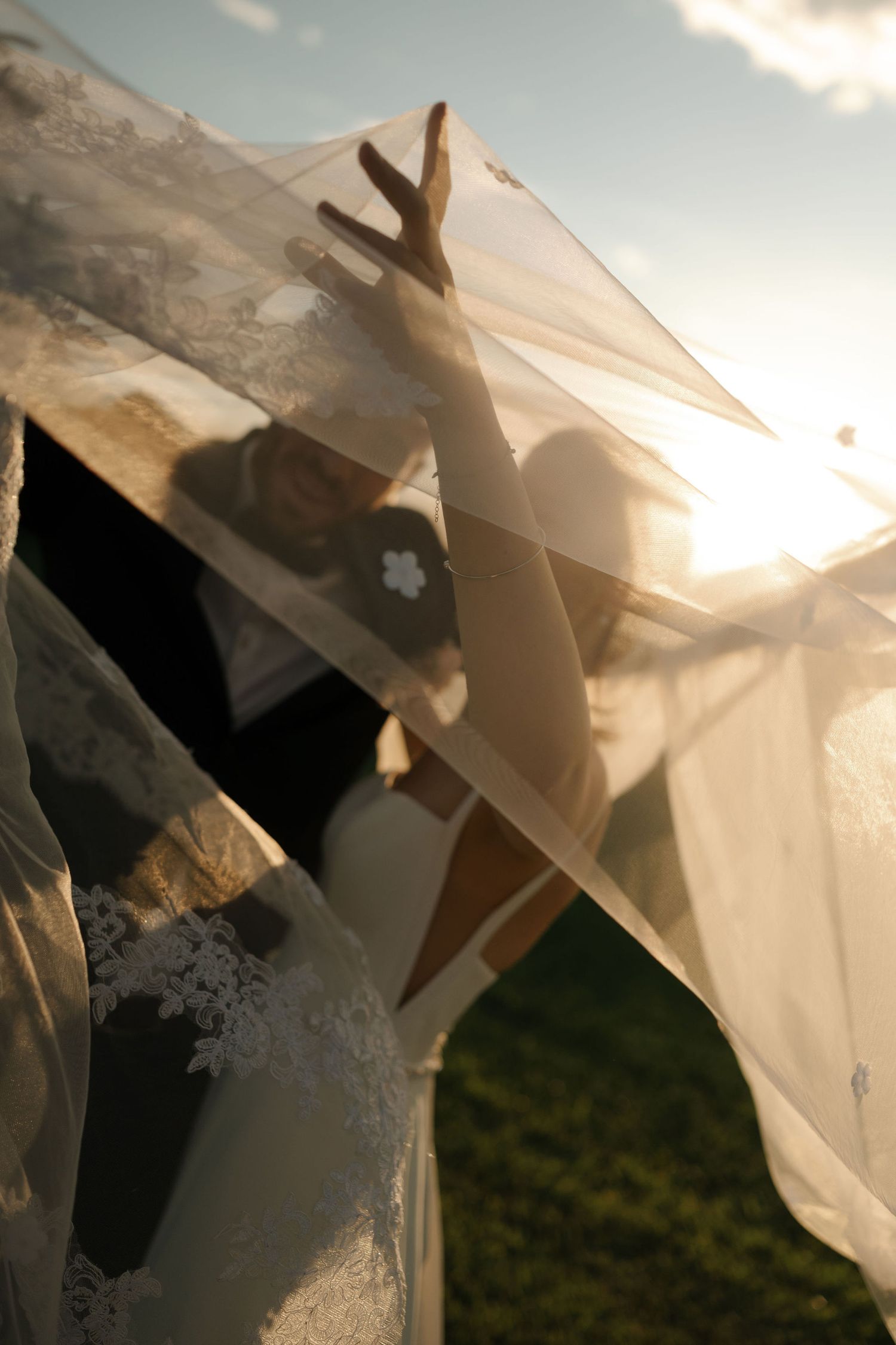 A hand reaches up through sheer fabric towards sunlight creating a dreamy silhouette against a bright sky.
