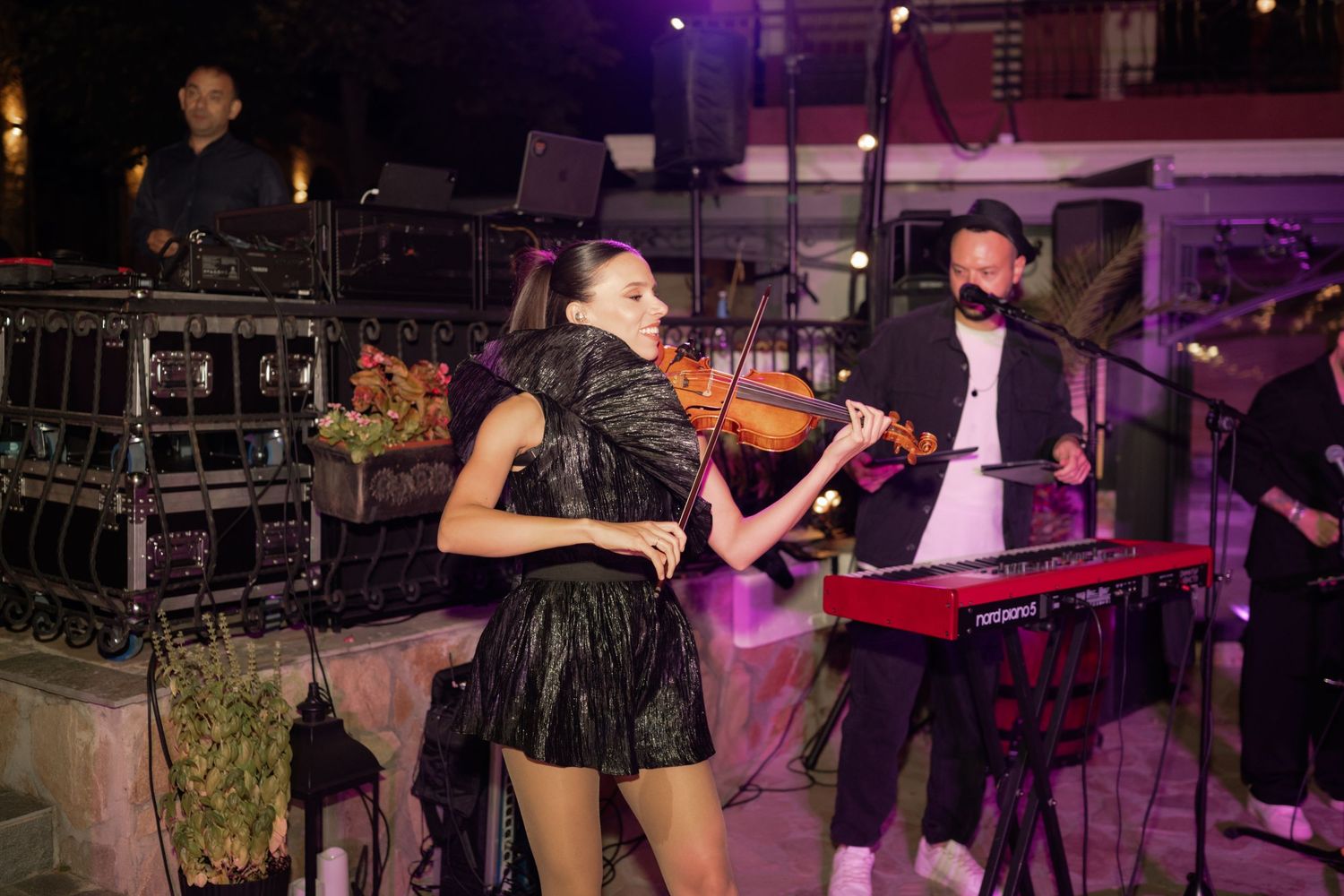 Musicians perform on stage with instruments during a nighttime concert with purple lighting and sound equipment.