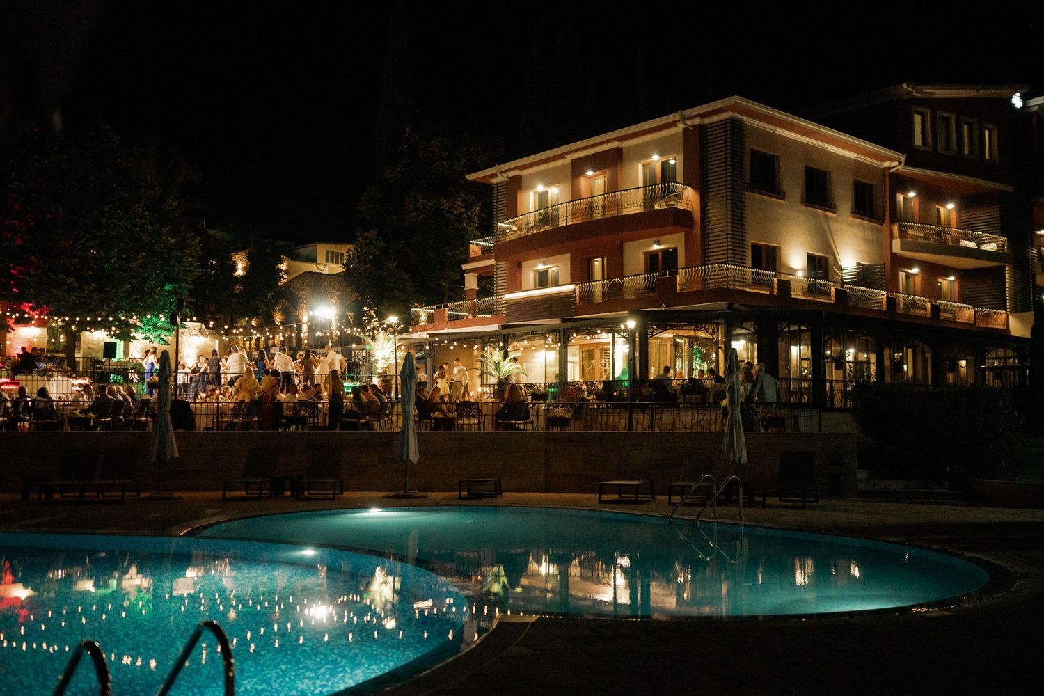 Illuminated resort pool and buildings at night with glowing blue water and warm lighting creating a tranquil atmosphere.