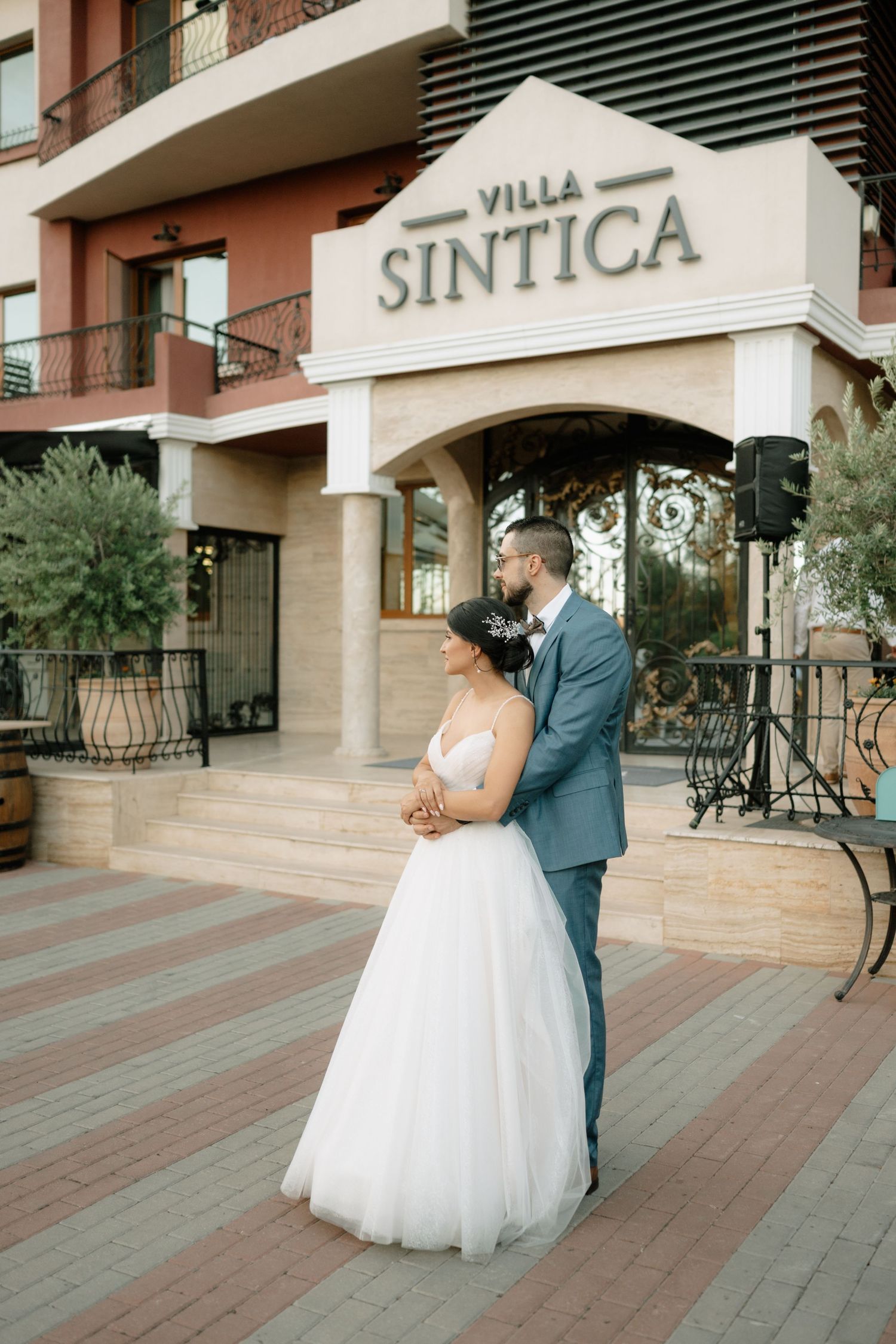 A couple in wedding attire embraces on a brick paved courtyard outside Villa Siena.