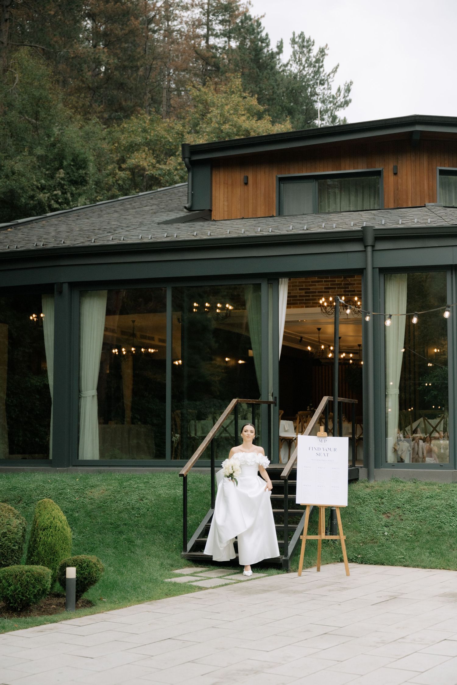 A modern wood-paneled event venue with large windows and string lights shown from multiple exterior angles in a natural setting.
