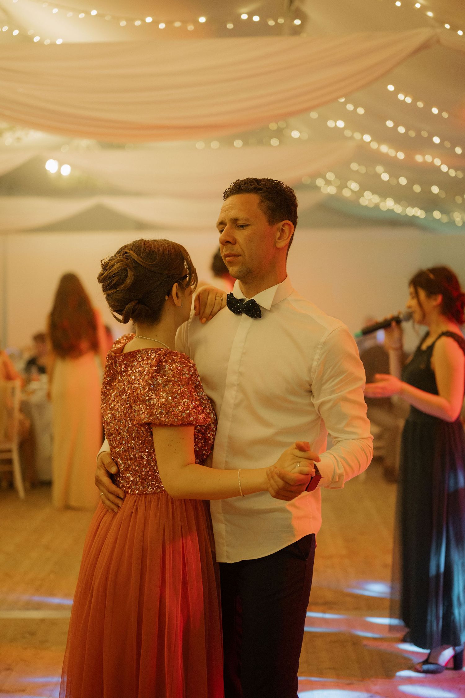 Couple sharing a romantic first dance at a wedding reception in a decorated venue with fairy lights.