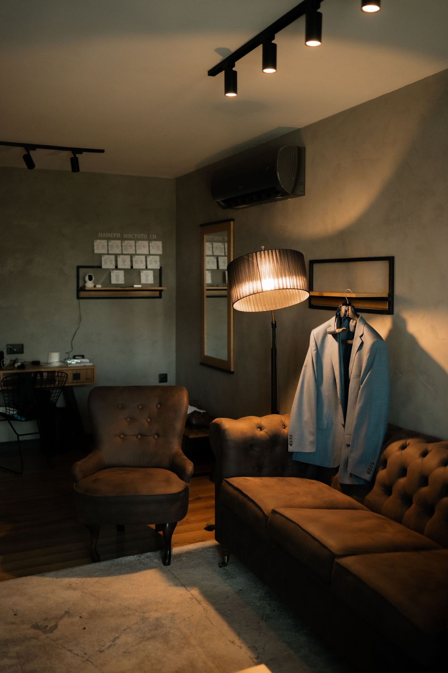 A cozy interior space with brown leather seating, track lighting, and a light blue jacket hanging under a modern lamp fixture.