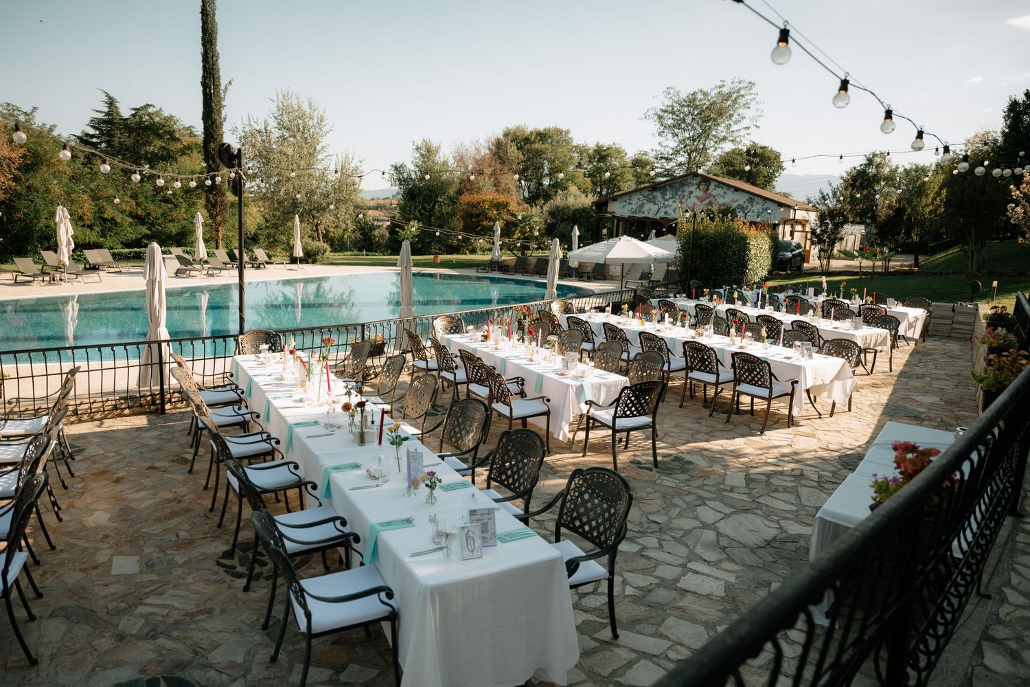 Outdoor wedding reception setup with long tables and string lights at dusk creating a romantic atmosphere.
