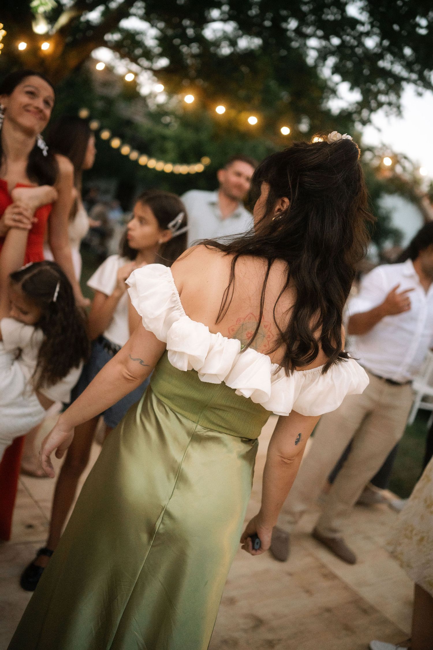 People dancing at an outdoor wedding celebration with string lights and natural lighting at dusk.