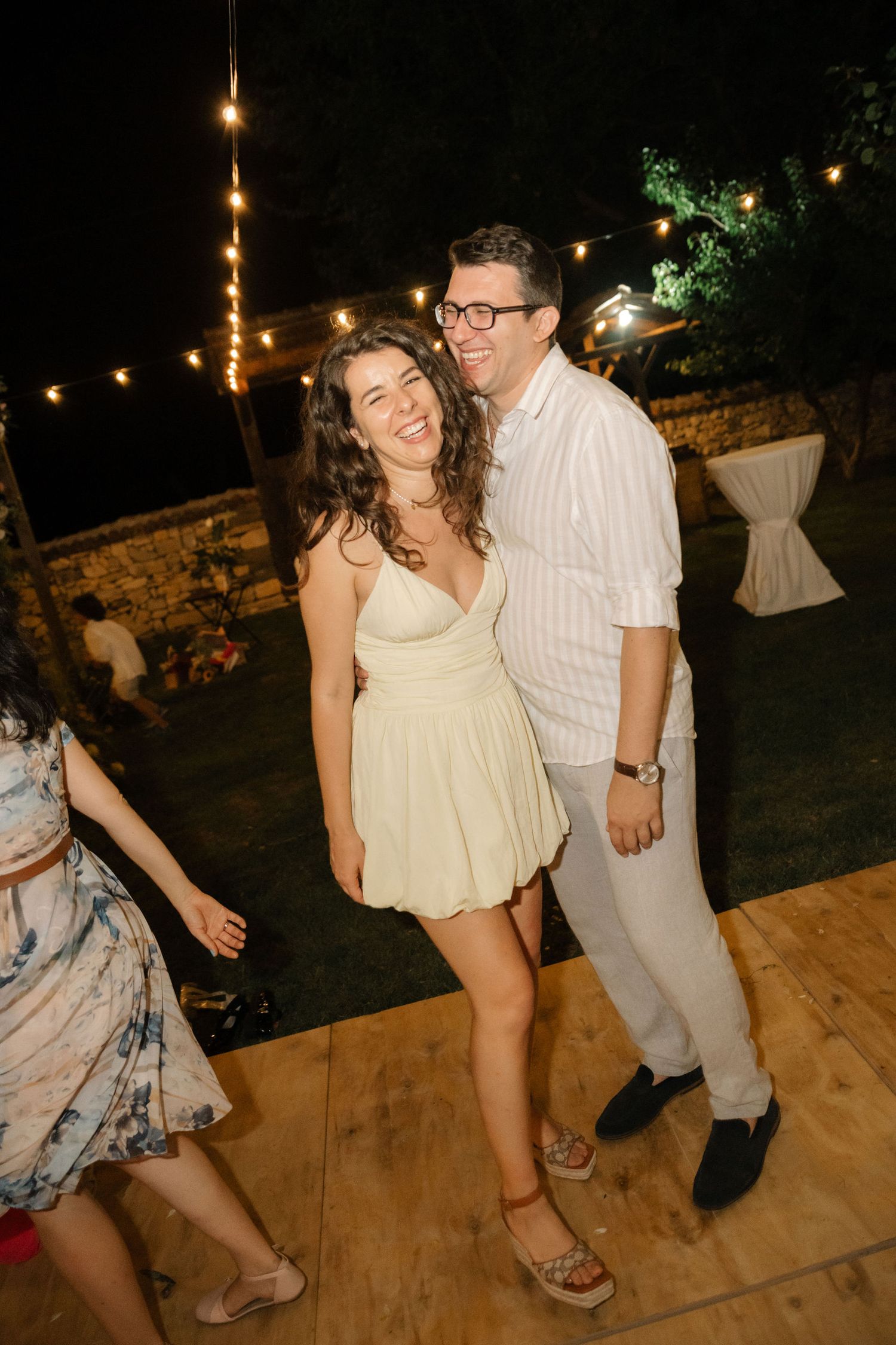 People dancing together on a wooden deck at night with string lights illuminating the outdoor space.