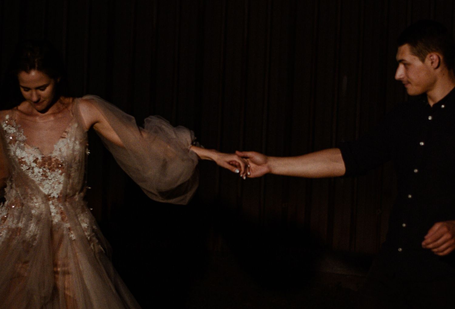 A couple dances intimately during their first dance at a dimly lit wedding reception.