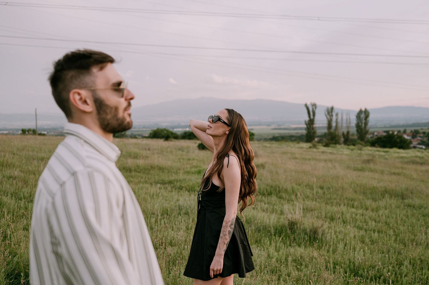 Couple shares intimate moments in a serene meadow with mountains in the background during golden hour.