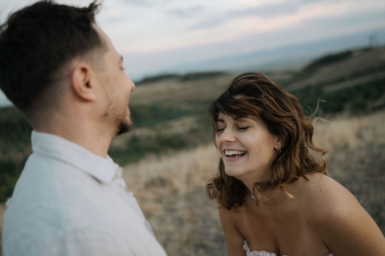 A couple shares a tender moment outdoors in a romantic mountainside setting at sunset.