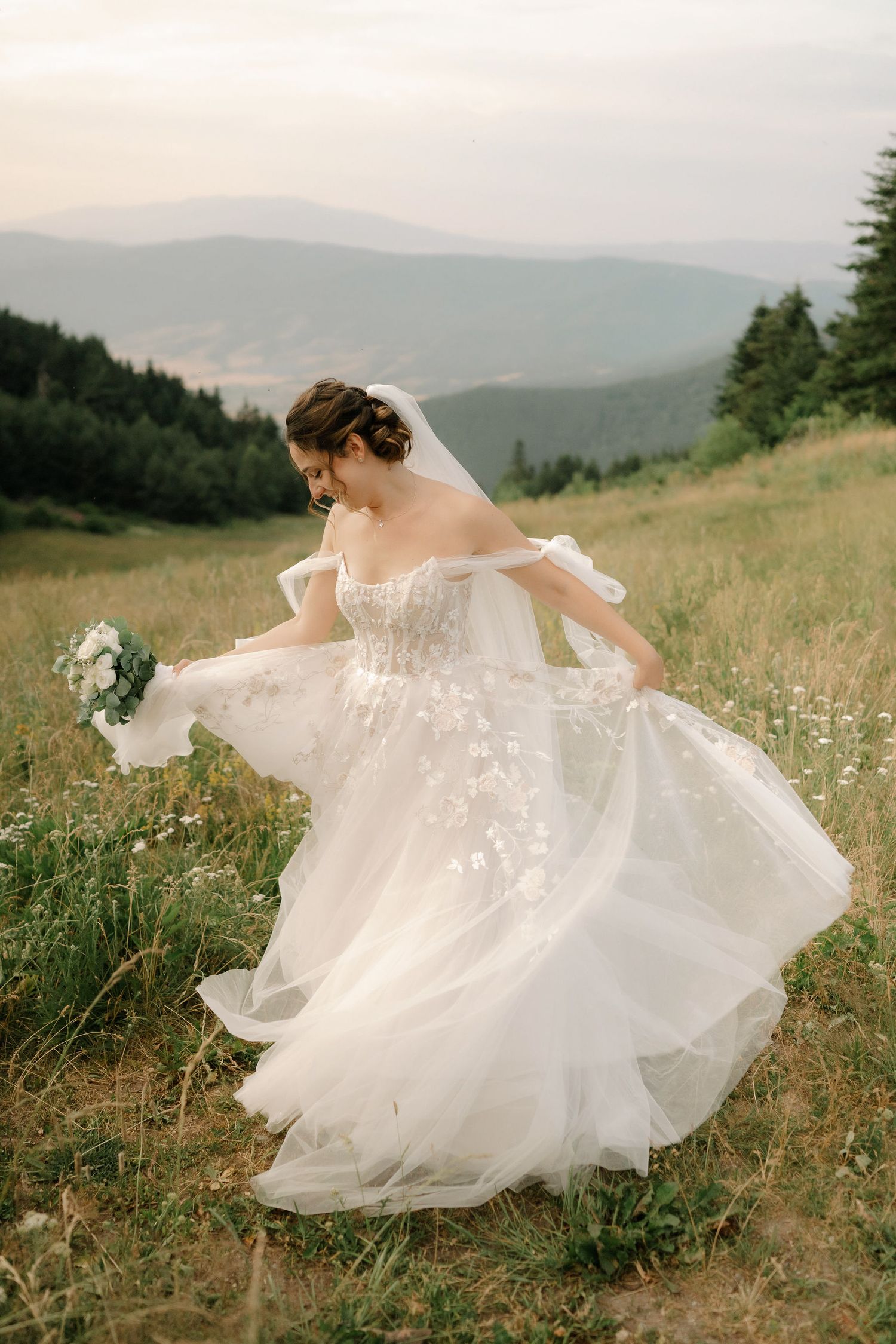A flowing white wedding dress twirls gracefully in a mountain meadow filled with wildflowers at sunset.