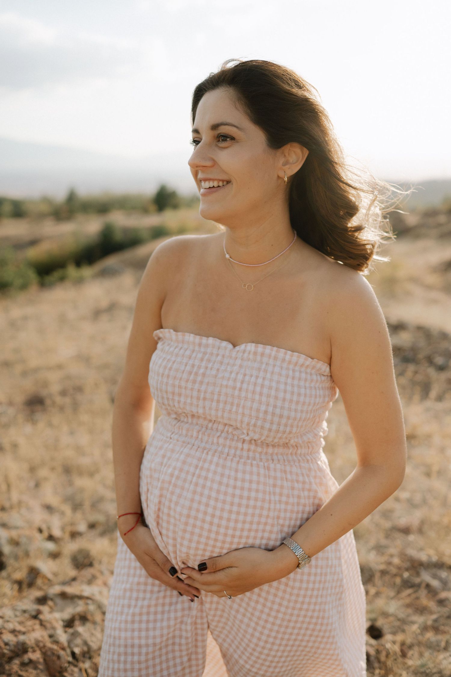 A person in a pink gingham dress poses in a desert landscape during golden hour.