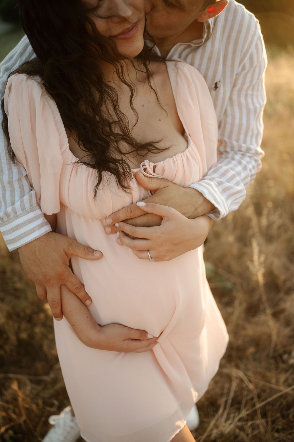 Intimate maternity portraits showing couple's tender moments in warm sunlight against natural outdoor backdrop.