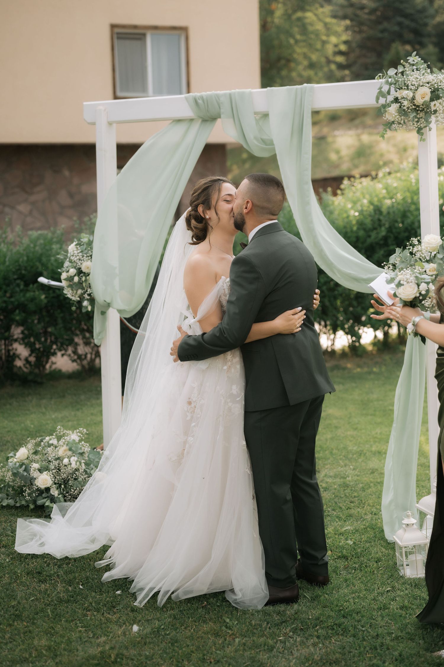 A wedding couple shares an intimate moment under flowing mint green curtains in an outdoor garden setting.
