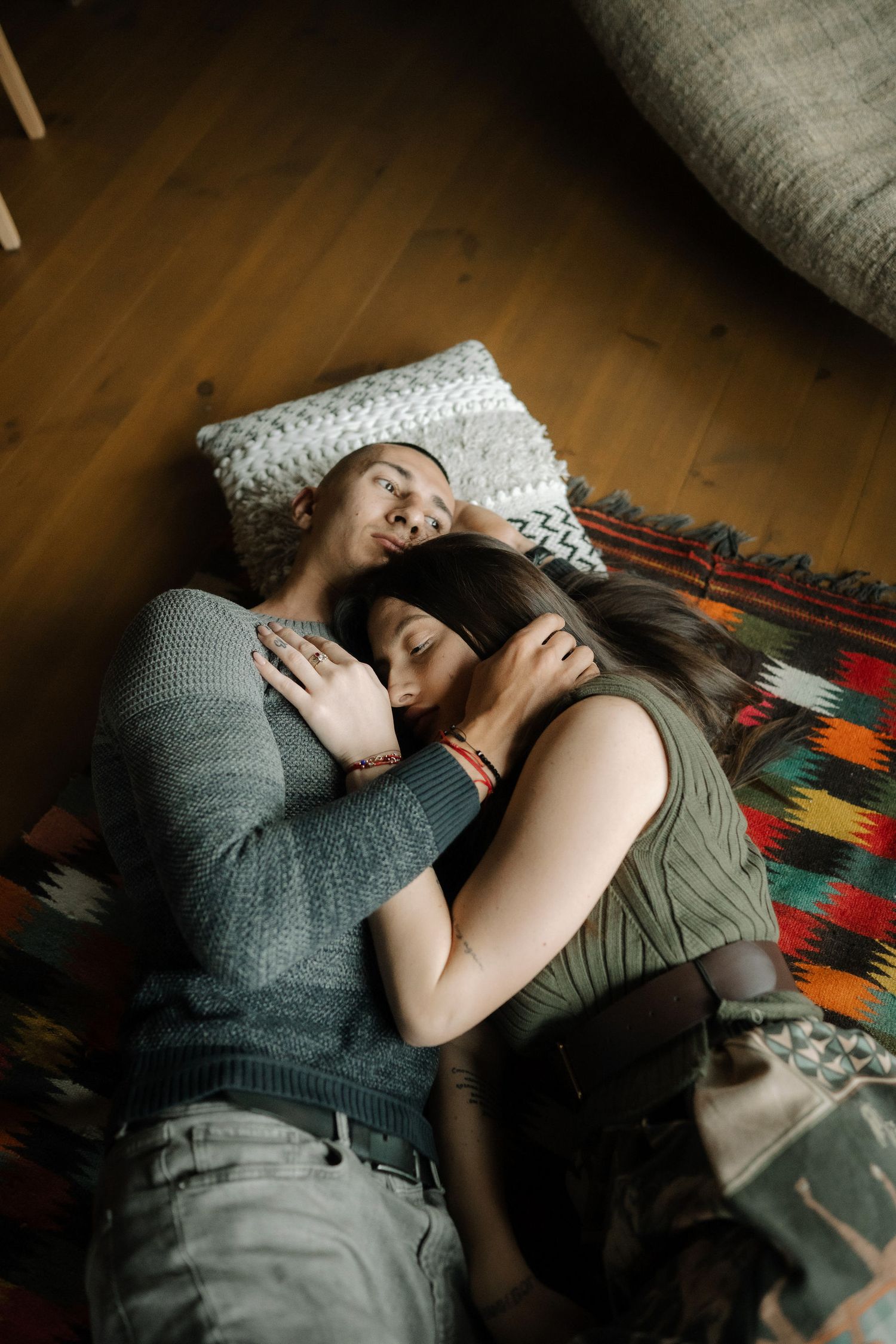 Two people lying close together on a colorful patterned rug in an intimate embrace.