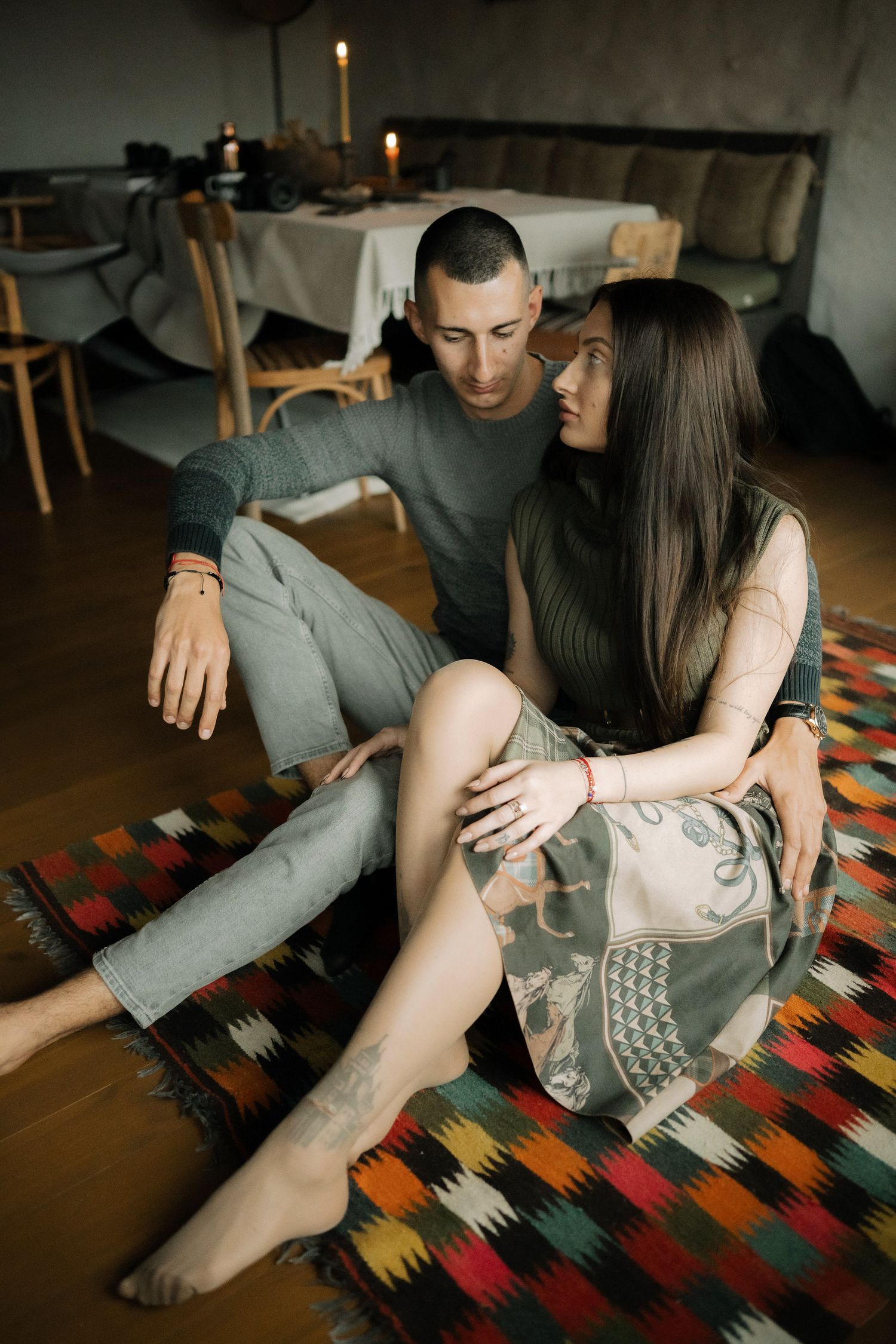 Two people sitting together on a colorful patterned rug in a dimly lit room.