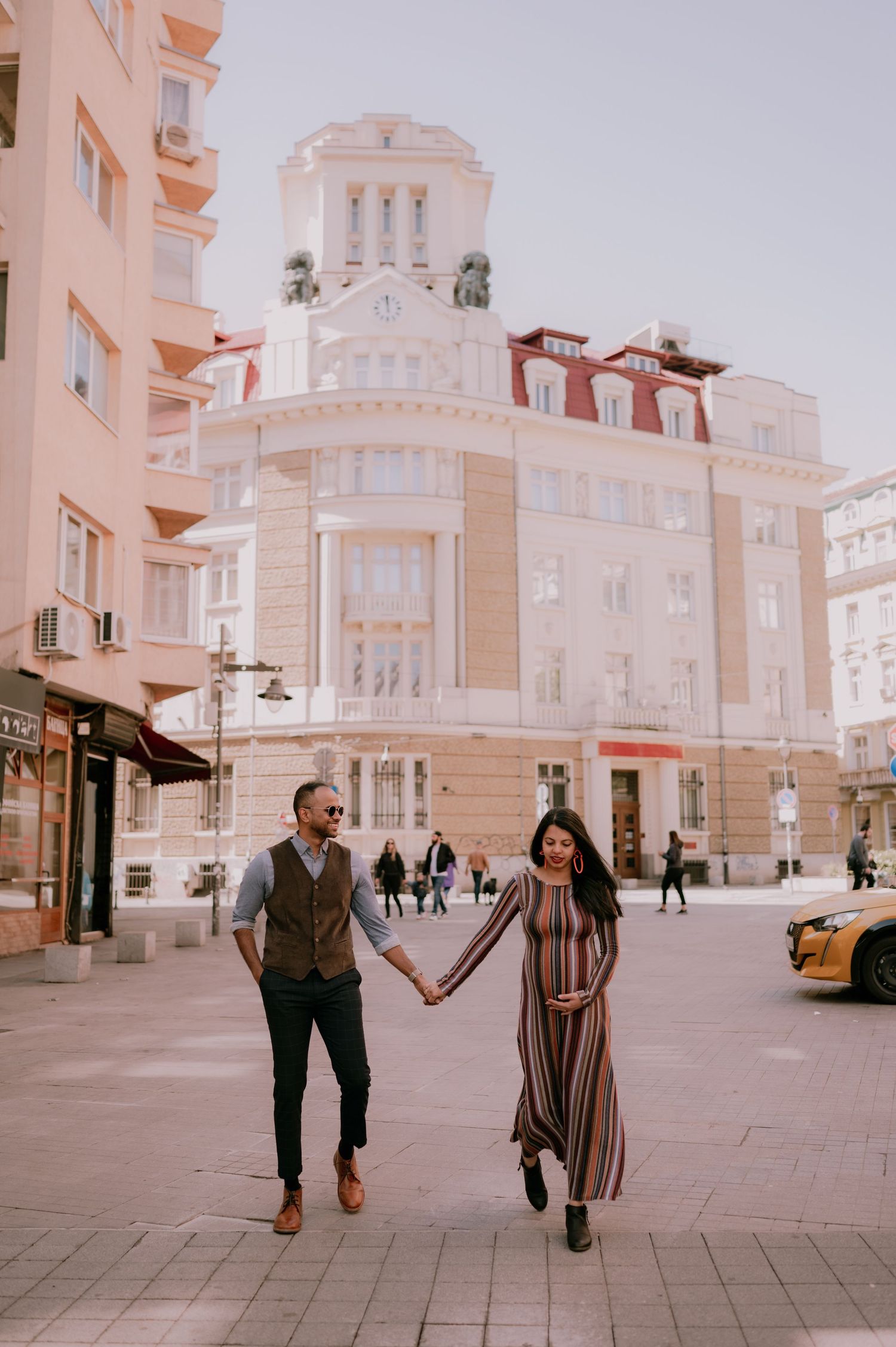 Couple holding hands walking in a European city square with elegant historic buildings in the background.