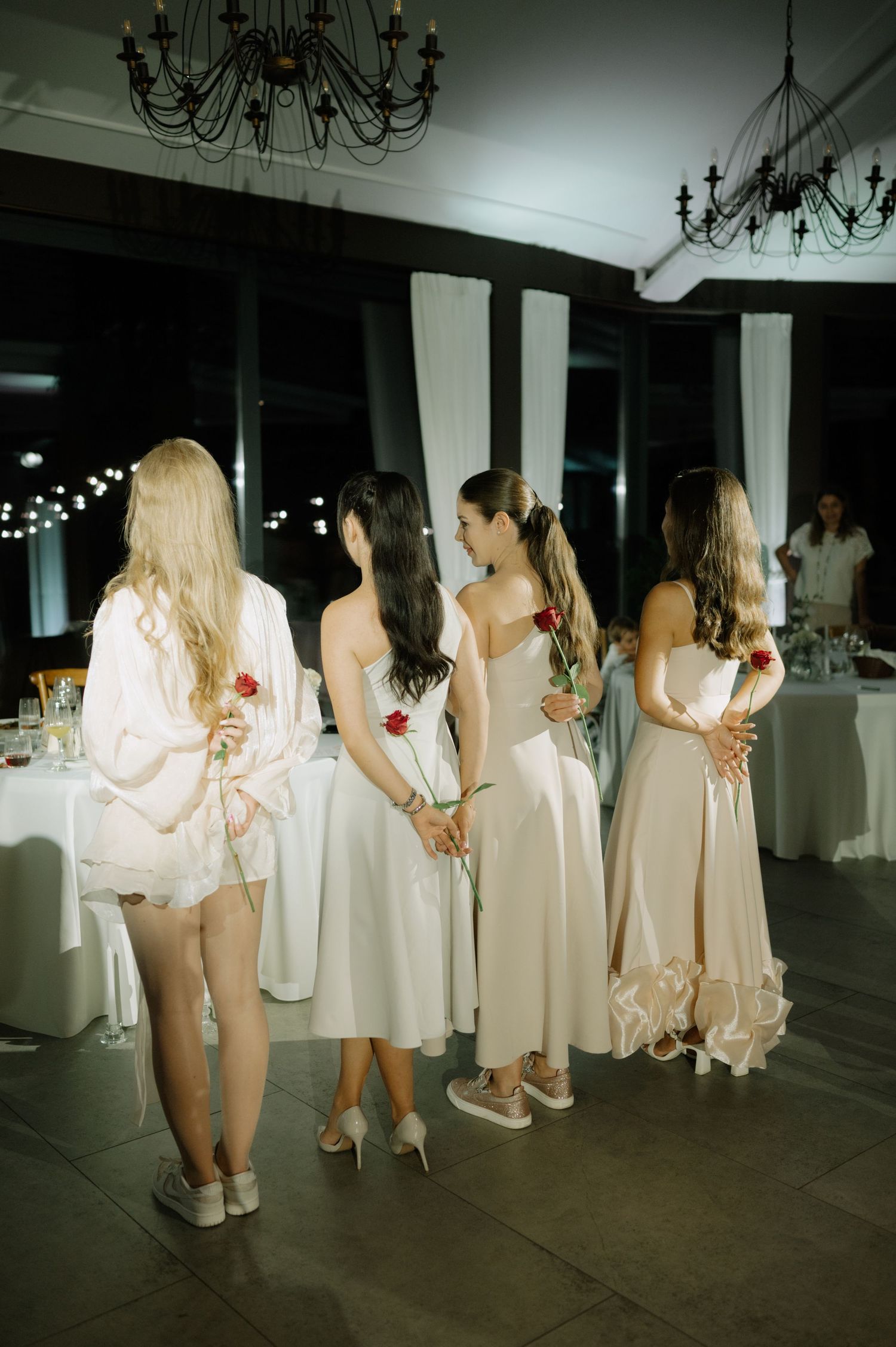 A group of people in white attire standing in line at an elegant indoor venue with chandeliers.