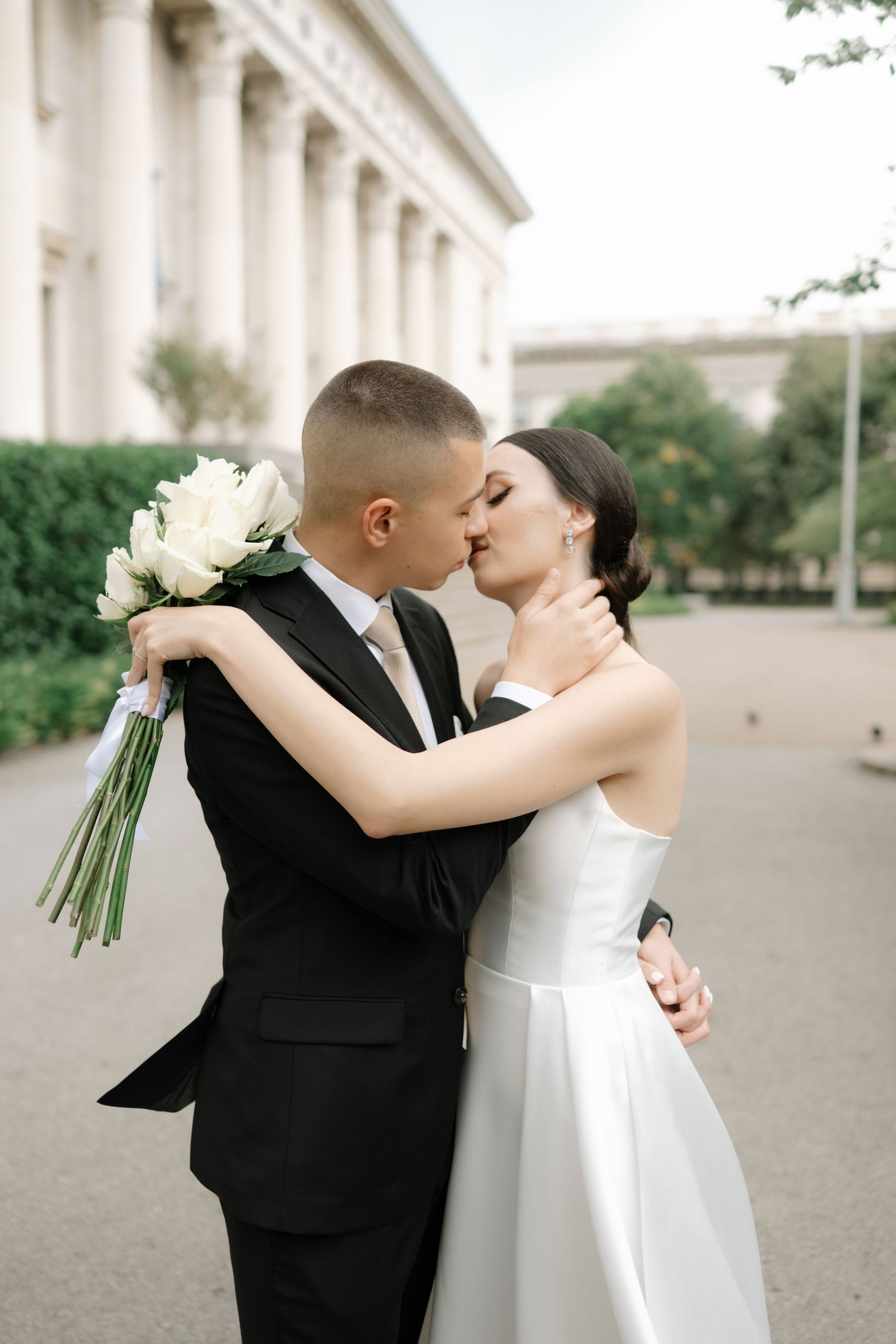 A romantic wedding couple shares tender kisses in four consecutive photos in front of a light colored building.